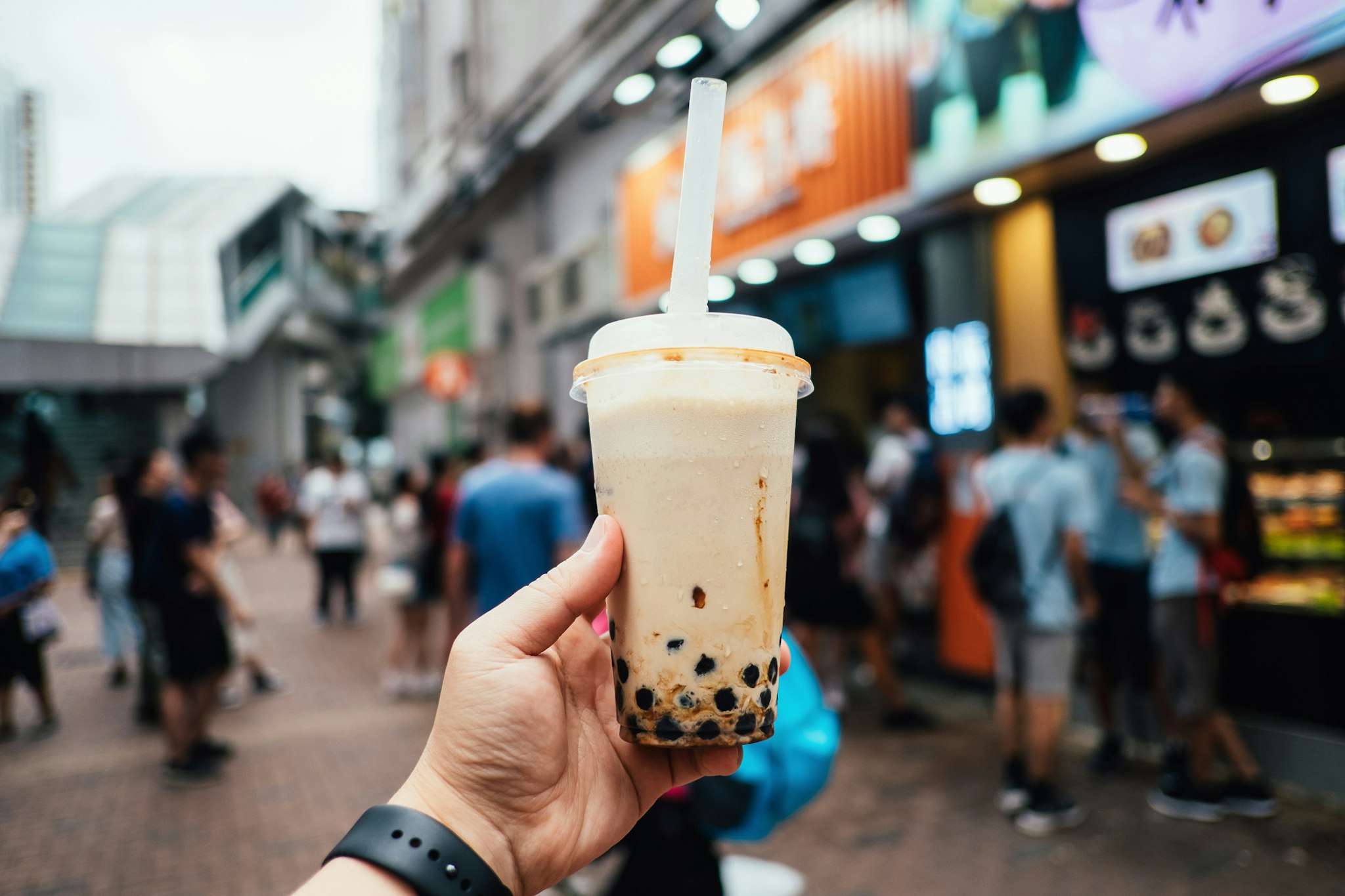 Human hand holding a bottle of iced cold bubble tea against city street in a hot summer day