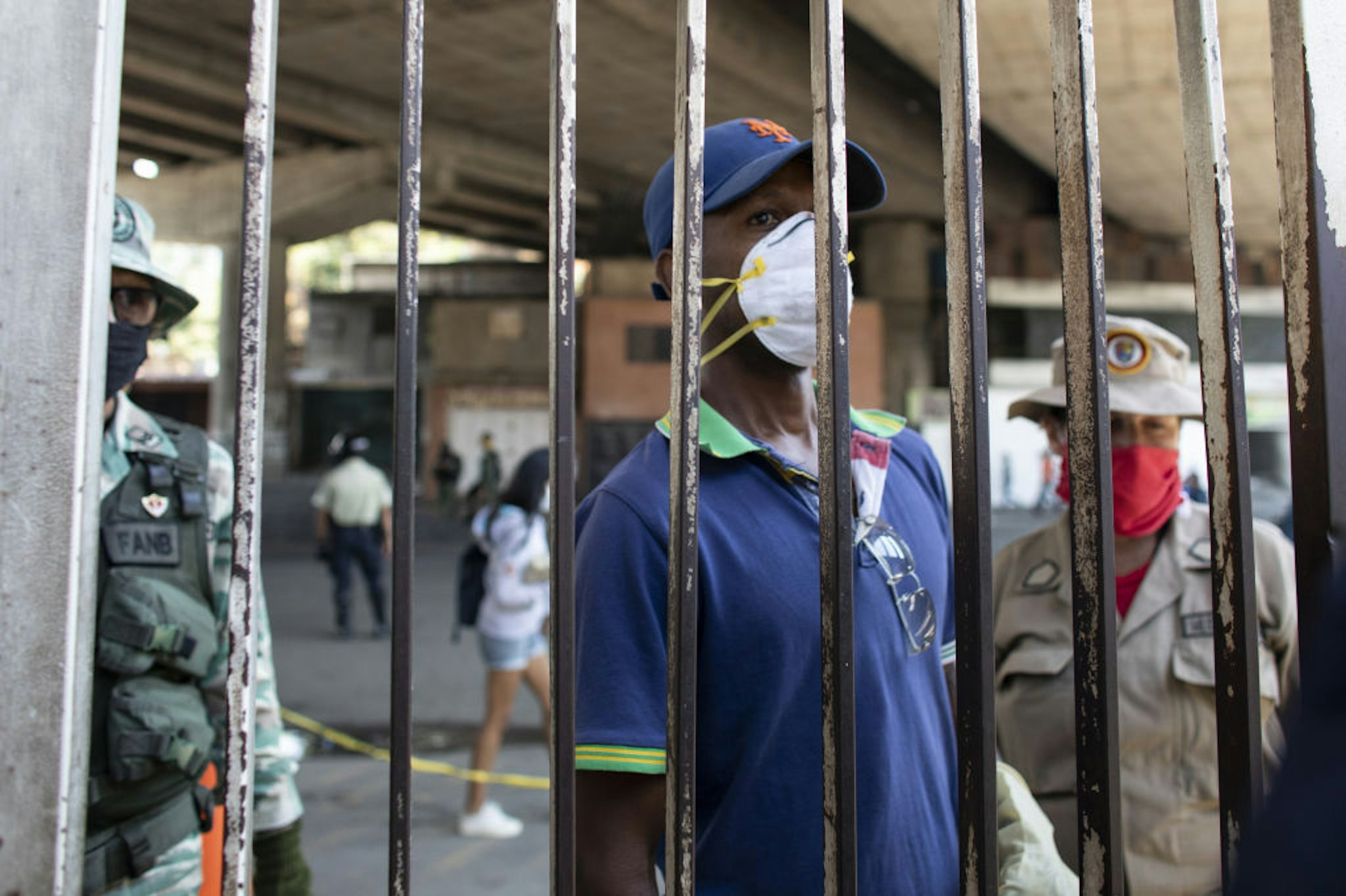 A person wearing a protective mask waits behind a security gate outside of the Ana Francisca Perez de Leon Hospital in the Petare neighborhood of Caracas, Venezuela, on Wednesday, April 15, 2020.