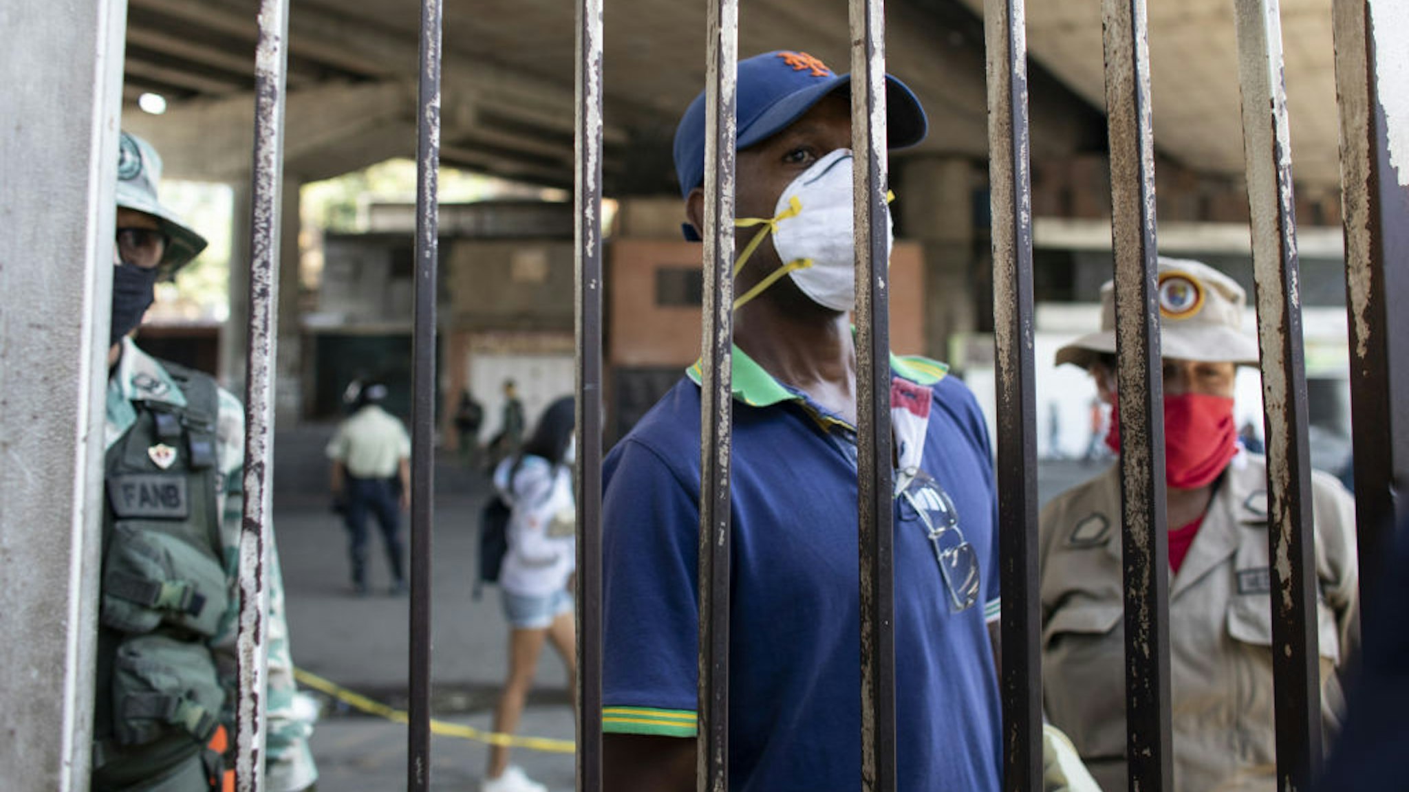 A person wearing a protective mask waits behind a security gate outside of the Ana Francisca Perez de Leon Hospital in the Petare neighborhood of Caracas, Venezuela, on Wednesday, April 15, 2020.