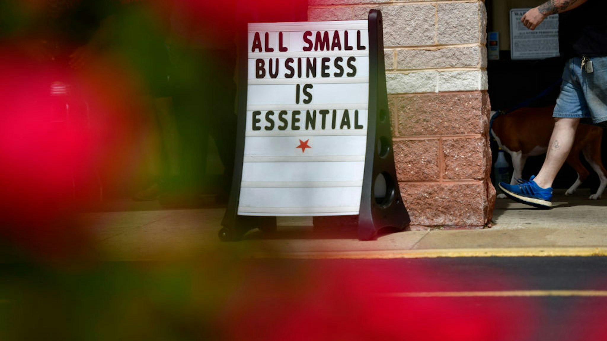 A man walks his dog past a placard stating "ALL SMALL BUSINESS IS ESSENTIAL" outside Atilis Gym on May 20, 2020 in Bellmawr, New Jersey.