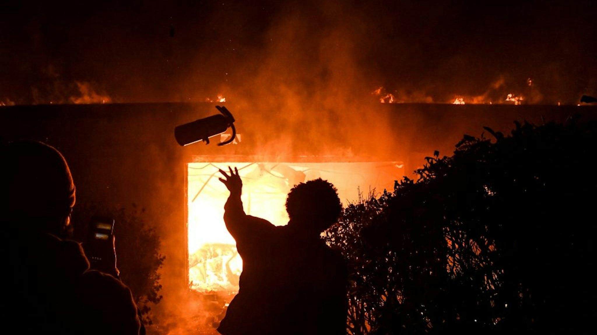 OPSHOT - A protester throws a fire extinguisher in a burning building during a demonstration in Minneapolis, Minnesota, on May 29, 2020, over the death of George Floyd, a black man who died after a white policeman kneeled on his neck for several minutes. - Violent protests erupted across the United States late on May 29 over the death of a handcuffed black man in police custody, with murder charges laid against the arresting Minneapolis officer failing to quell seething anger. (Photo by Chandan KHANNA / AFP) (Photo by CHANDAN KHANNA/AFP via Getty Images)
