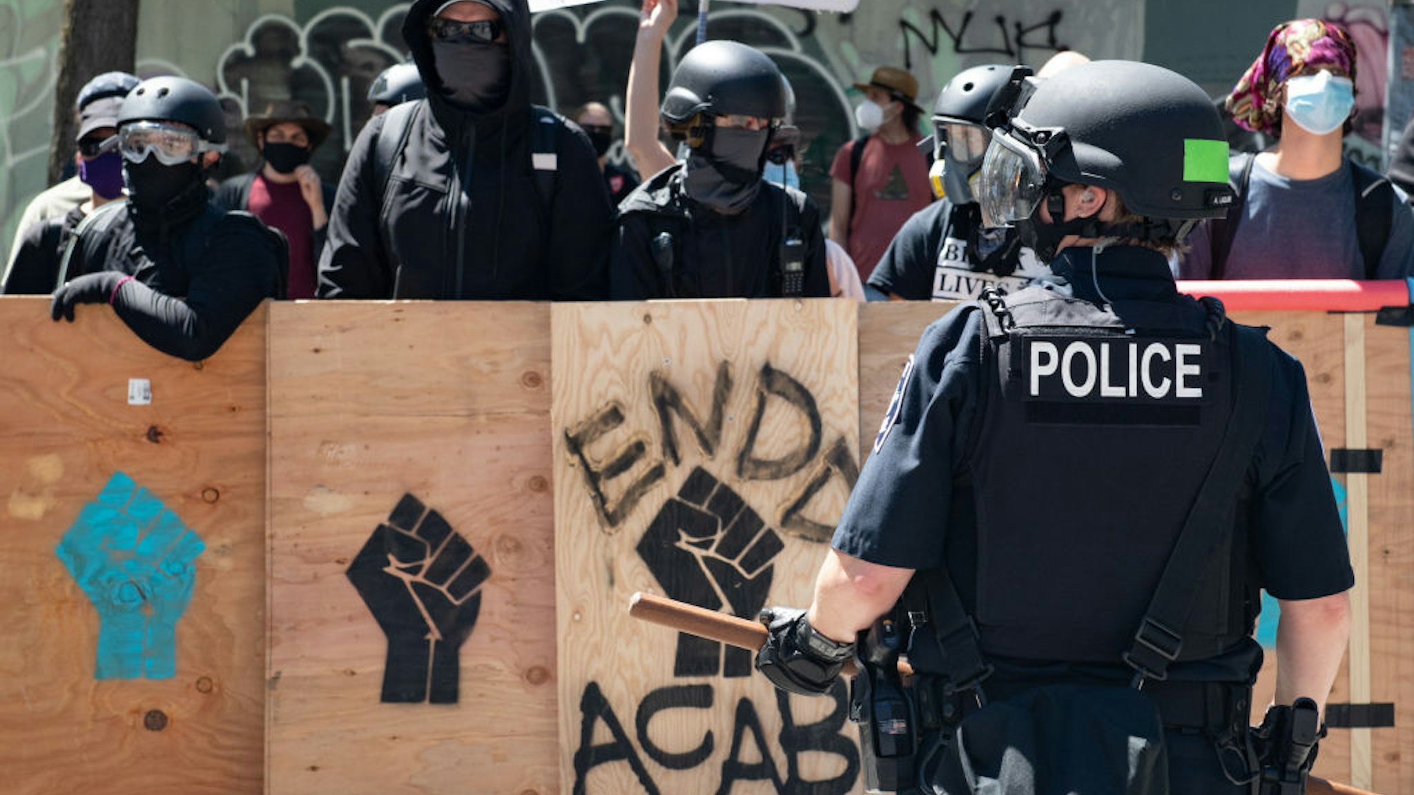 A police officer stands in front of counter protesters during the Seattle Police Officers Guildâs rally to stop defunding of the Seattle Police Department on Sunday, August 9, 2020 at Seattle City Hall.