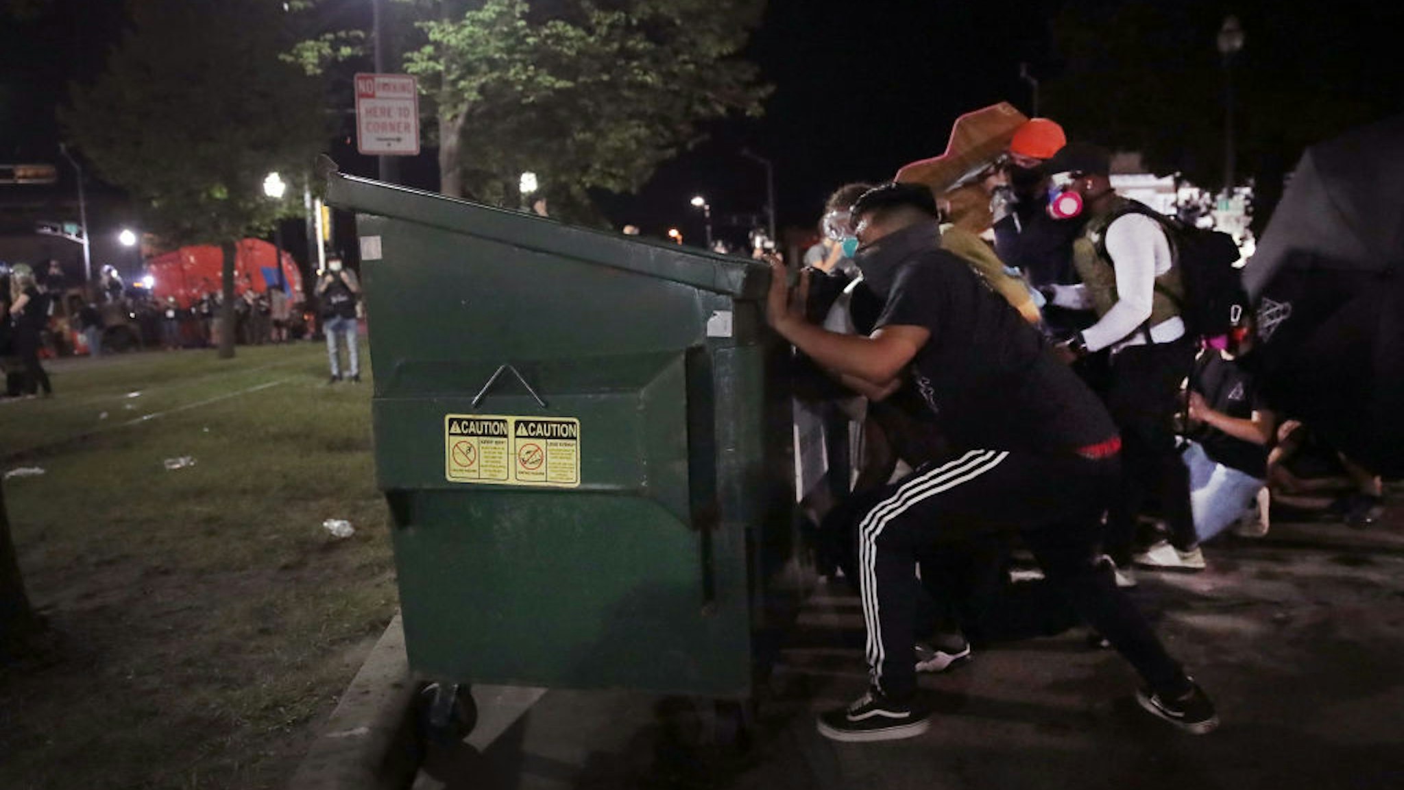 Protesters take cover behind a dumpster as they confront police in front of the Kenosha County Courthouse during a third night of unrest on August 25, 2020 in Kenosha, Wisconsin.