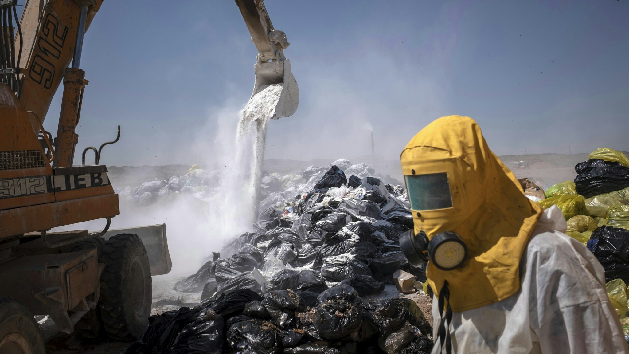 An Iranian worker wearing a protective suit as a loader covers infectious wastes with lime in Tehran Garbage Disposal Center, following the new coronavirus disease (COVID-19) outbreak in Iran, June 7, 2020.
