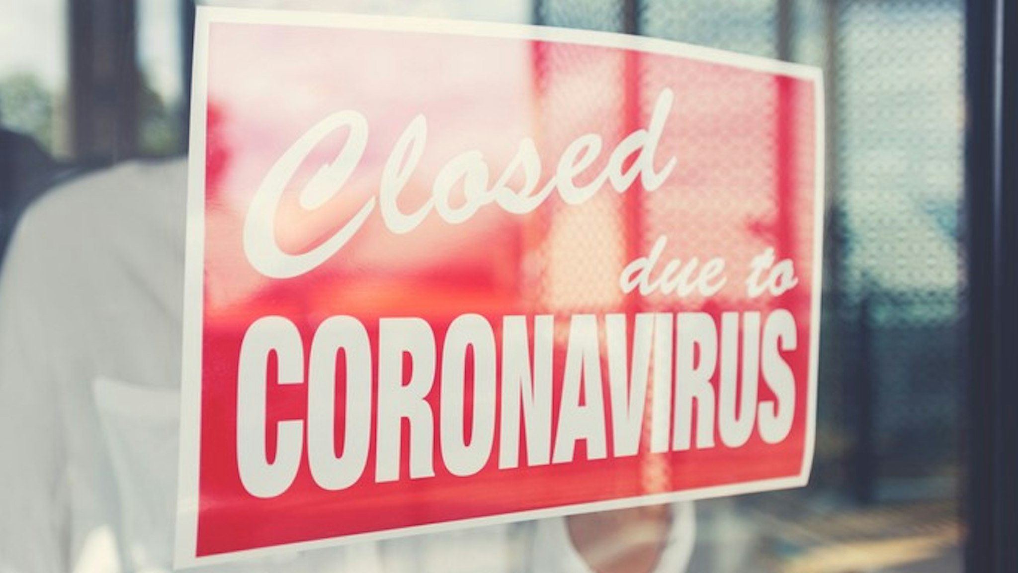 Store owner putting up a closed sign in the window. Sign says: closed due to coronavirus