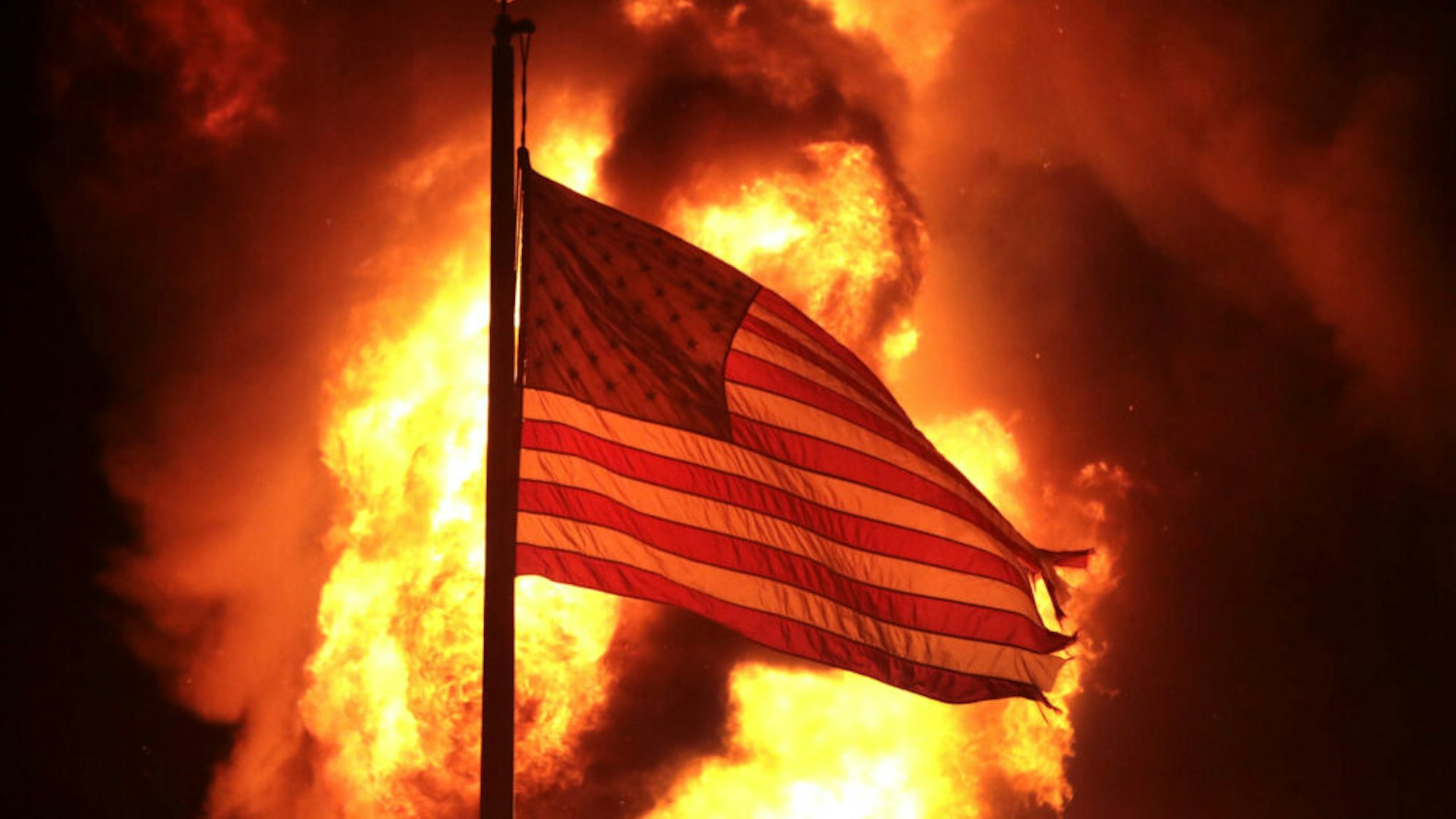 A flag flies in front of a department of corrections building after it was set ablaze during a second night of rioting on August 24, 2020 in Kenosha, Wisconsin. Rioting as well as clashes between police and protesters began Sunday night after a police officer shot Jacob Blake 7 times in the back in front of his three children.