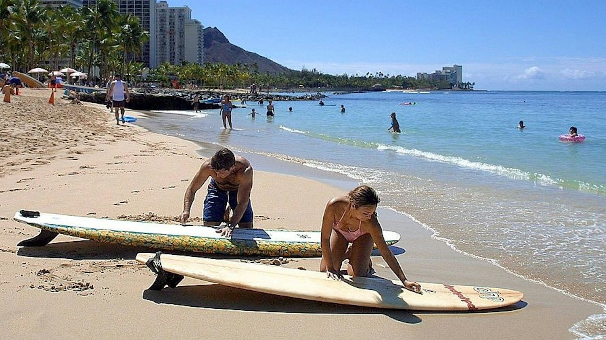 WAIKIKI, UNITED STATES: Scott Herson (L) and Marilyn Shepard (R) of Manhattan Beach, California, wax their surfboards 06 September 2001 on Waikiki Beach in Hawaii near where sharks were sited 05 September afternoon which closed the world famous beach until after sunset. Lifeguards and the crew of a low-flying helicopter used bullhorns to order hundreds of beach goers out of the water after three sharks were spotted, 50 meters from the shore. While there have been no recent shark attacks in Hawaii, the decision to evacuate the beach is indicative of the widespread alarm in the United States of sharks following several recent deadly attacks. The beach reopened after authorities determined that the 9-foot black-tip sharks had left the area. AFP PHOTO/Mike NELSON (Photo credit should read