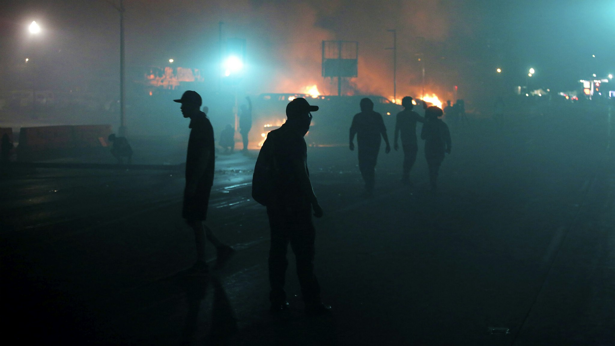 KENOSHA, WI - AUGUST 24: People walk trough smoke filled street from near by burinng buildings as demonstrators protest the police shooting of Jacob Blake on Monday, August 24, 2020 in Kenosha, Wisconsin. Blake was shot in the back multiple times by police officers responding to a domestic dispute call yesterday.