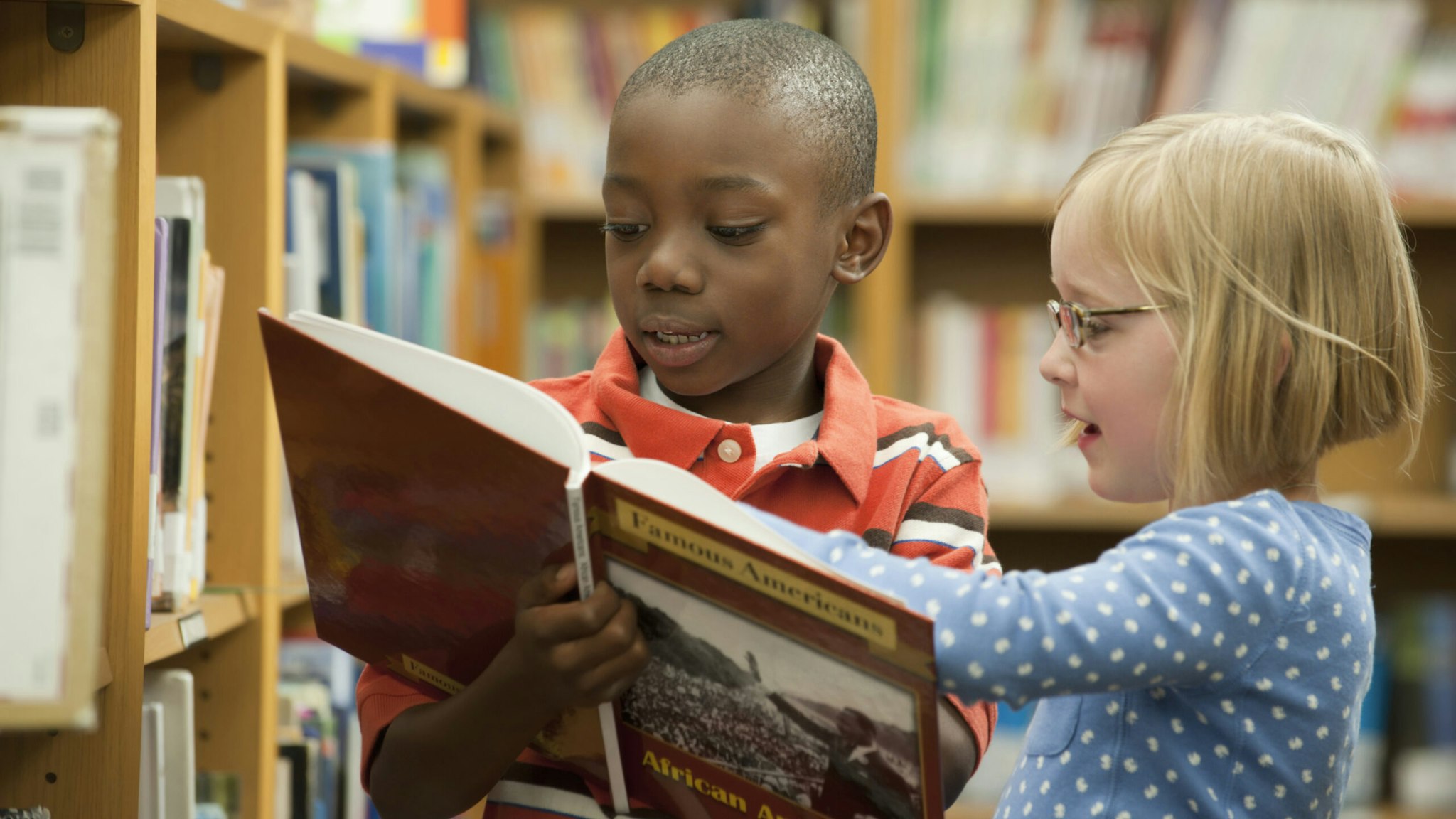 Boy and girl classmates sharing book in library