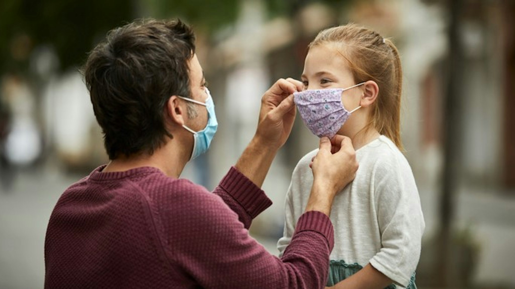 Father with surgical face mask, is putting a hand made protective face mask on his little daughter for the COVID-19 pandemic.