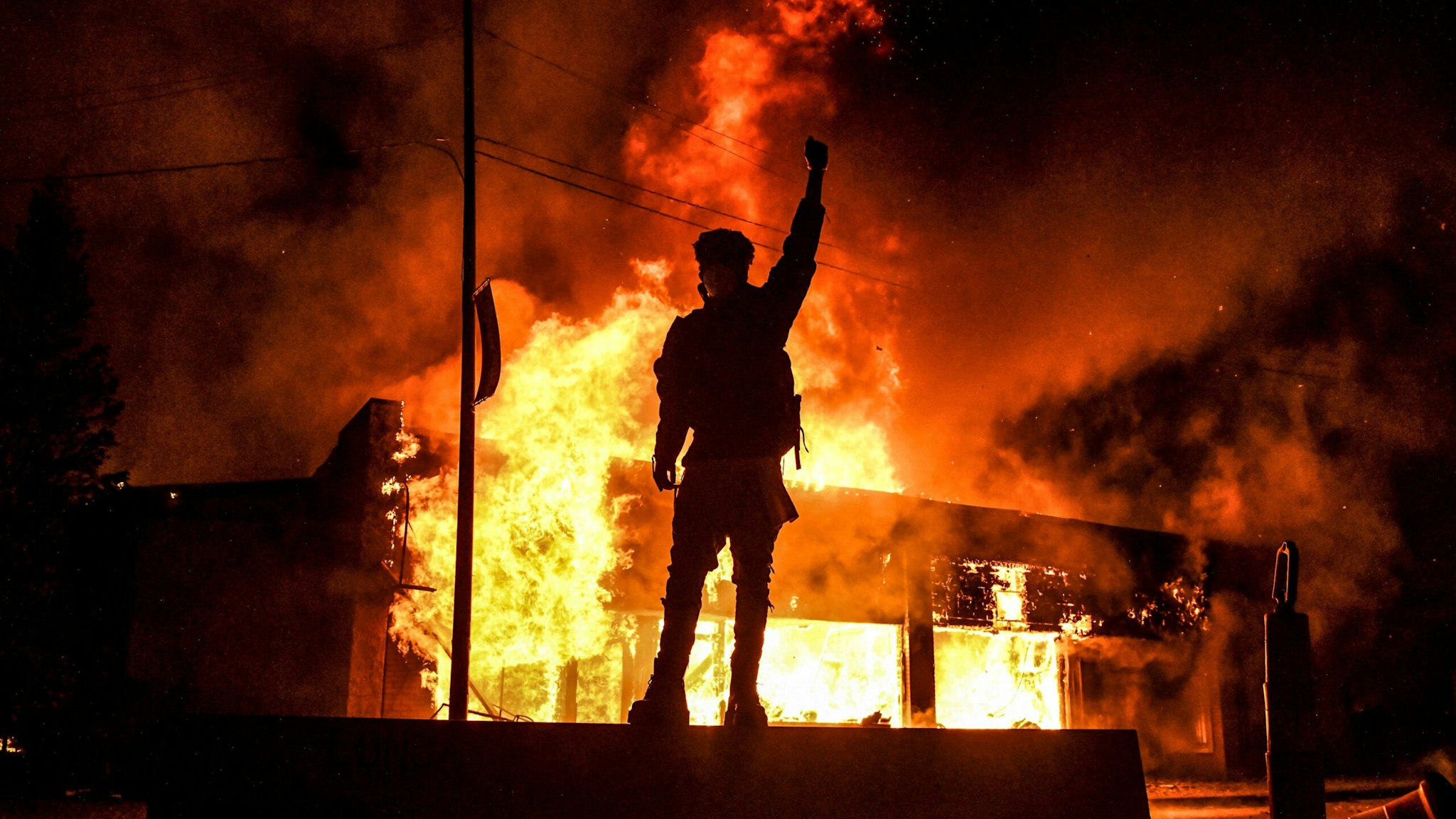 TOPSHOT - A protester reacts standing in front of a burning building set on fire during a demonstration in Minneapolis, Minnesota, on May 29, 2020, over the death of George Floyd, a black man who died after a white policeman kneeled on his neck for several minutes. - Violent protests erupted across the United States late on May 29 over the death of a handcuffed black man in police custody, with murder charges laid against the arresting Minneapolis officer failing to quell seething anger.