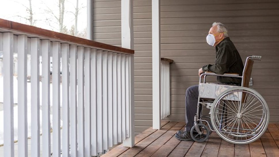Senior man in wheelchair wearing protective mask to prevent coronavirus transmission on porch