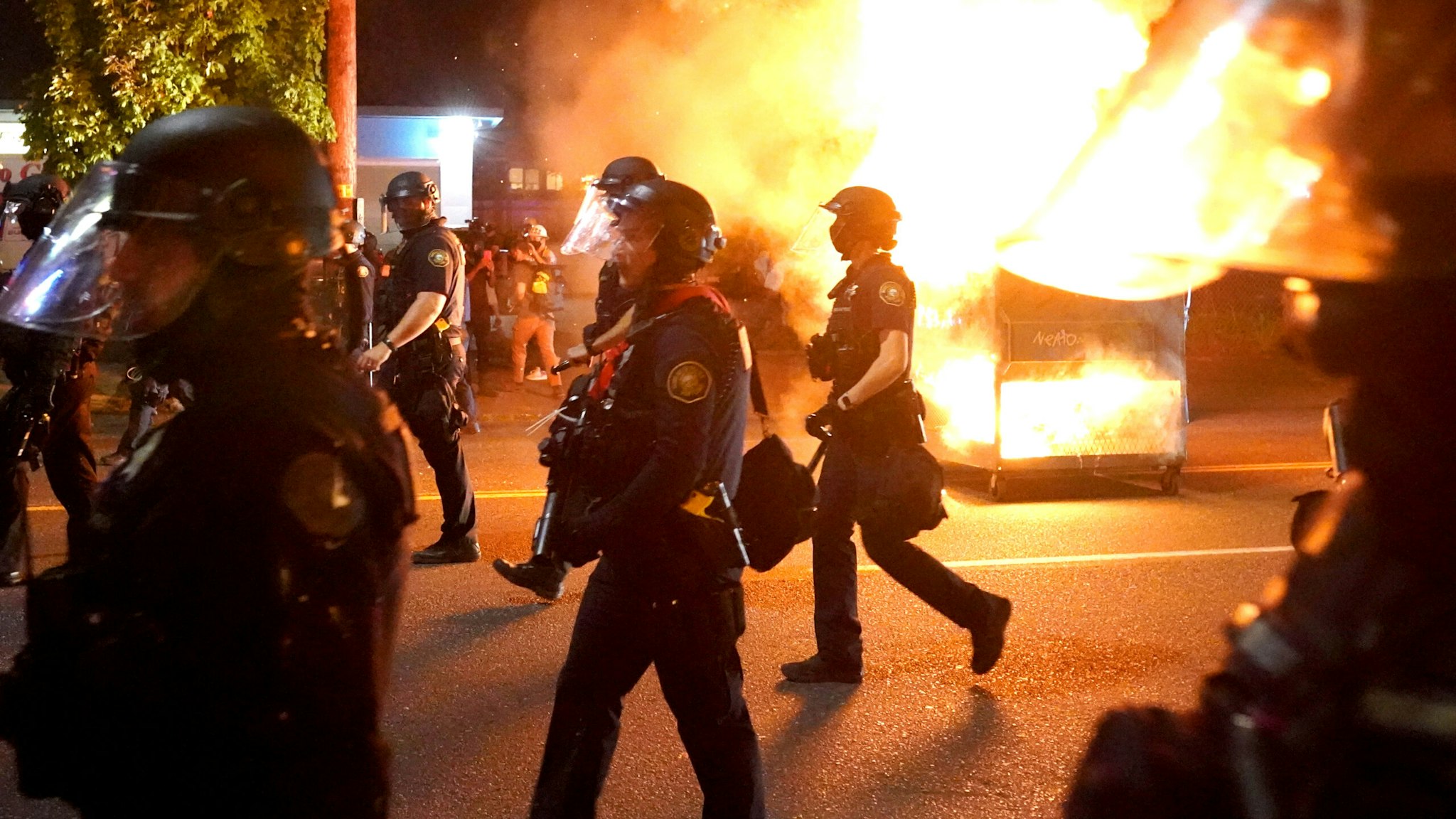 PORTLAND, OR - AUGUST 14: Portland police walk past a dumpster fire during a crowd dispersal on August 14, 2020 in Portland, Oregon. The Portland Police Bureau changed tactics Friday night, blocking streets well before the protest of about 400 people could reach the Portland Police Association building.