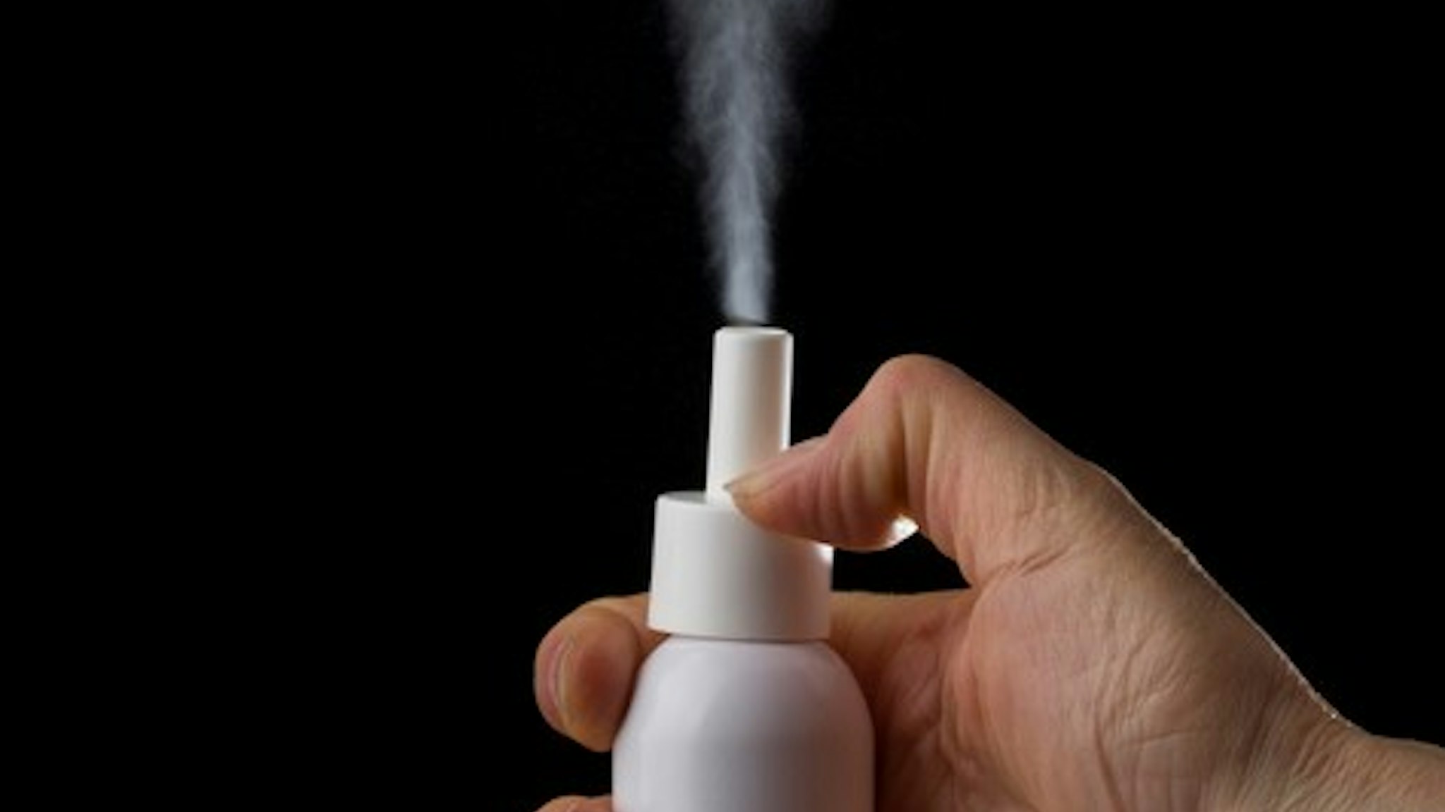 White container of spray bottle on black background. Hand holds medical inhaler