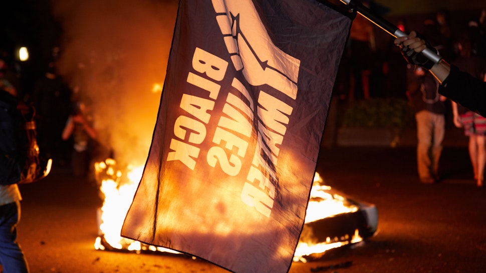 A Black Lives Matter flag waves in front of a fire at the North Precinct Police building in Portland, Oregon on September 6, 2020. - Protestors are marching for an end to racial inequality and police violence. Aaron Danielson, 39, a supporter of a far-right group called Patriot Prayer, was fatally shot August 29, 2020, in Portland, Oregon after he joined pro-Trump supporters who descended on the western US city, sparking confrontations with Black Lives Matter counter-protesters.
