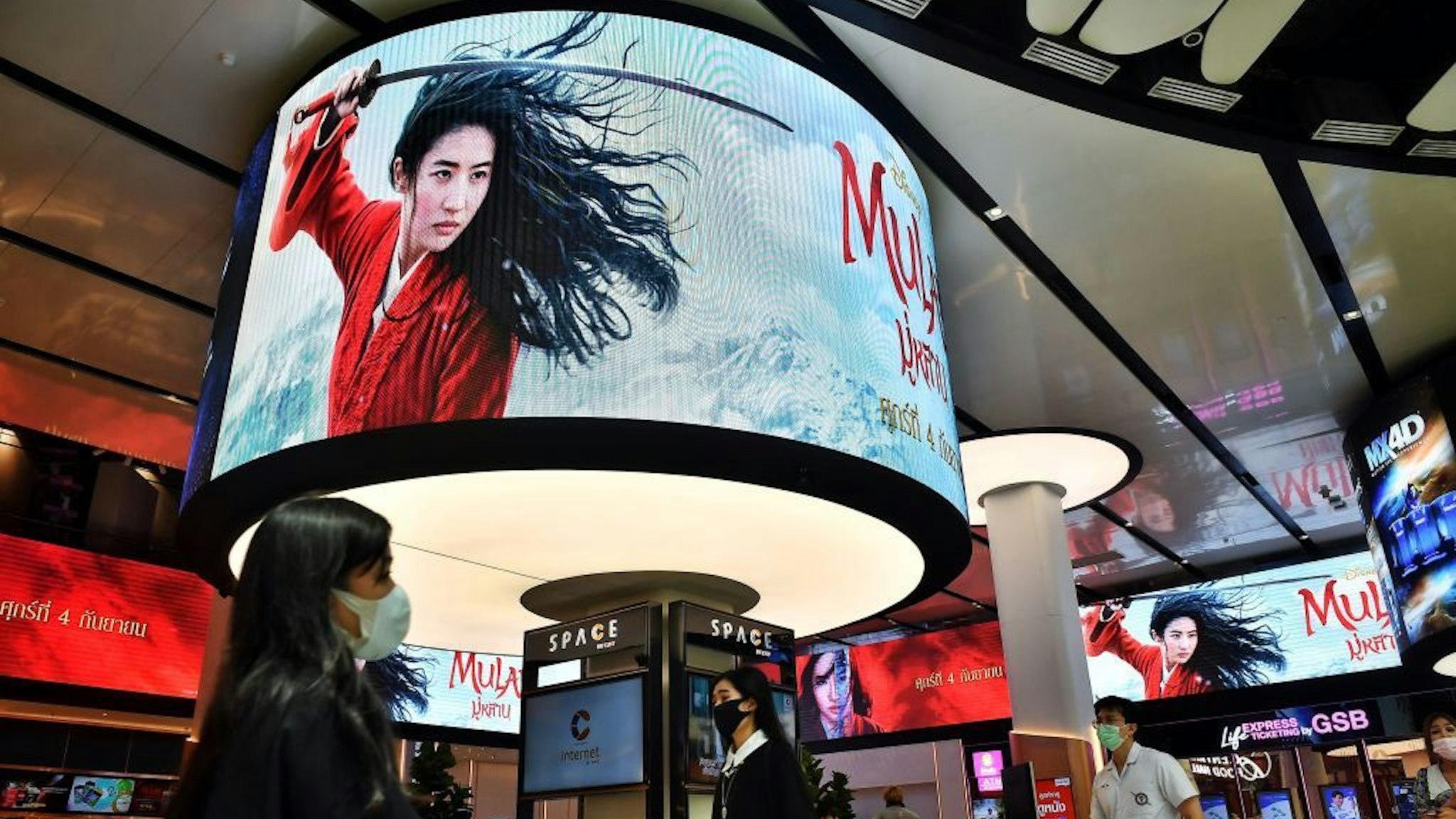 People walk past advertising displays for Disneys Mulan film at a cinema inside a shopping mall in Bangkok on September 8, 2020. - Disney's "Mulan" remake is facing fresh boycott calls after it emerged some of the blockbuster was filmed in China's Xinjiang, where widespread rights abuses against the region's Muslim population have been widely documented. (Photo by Lillian SUWANRUMPHA / AFP)