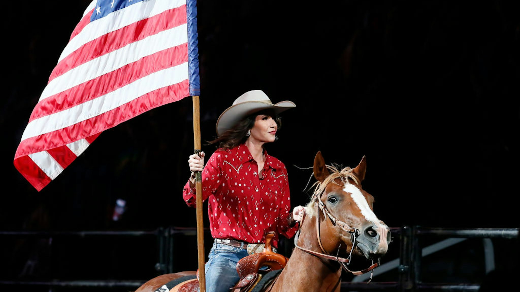 South Dakota's Governor Kristi Noem holds the U.S flag riding a horse during the Monster Energy Team Challenge, on July 11, 2020, at the Denny Sanford PREMIER Center, Sioux Falls, SD.