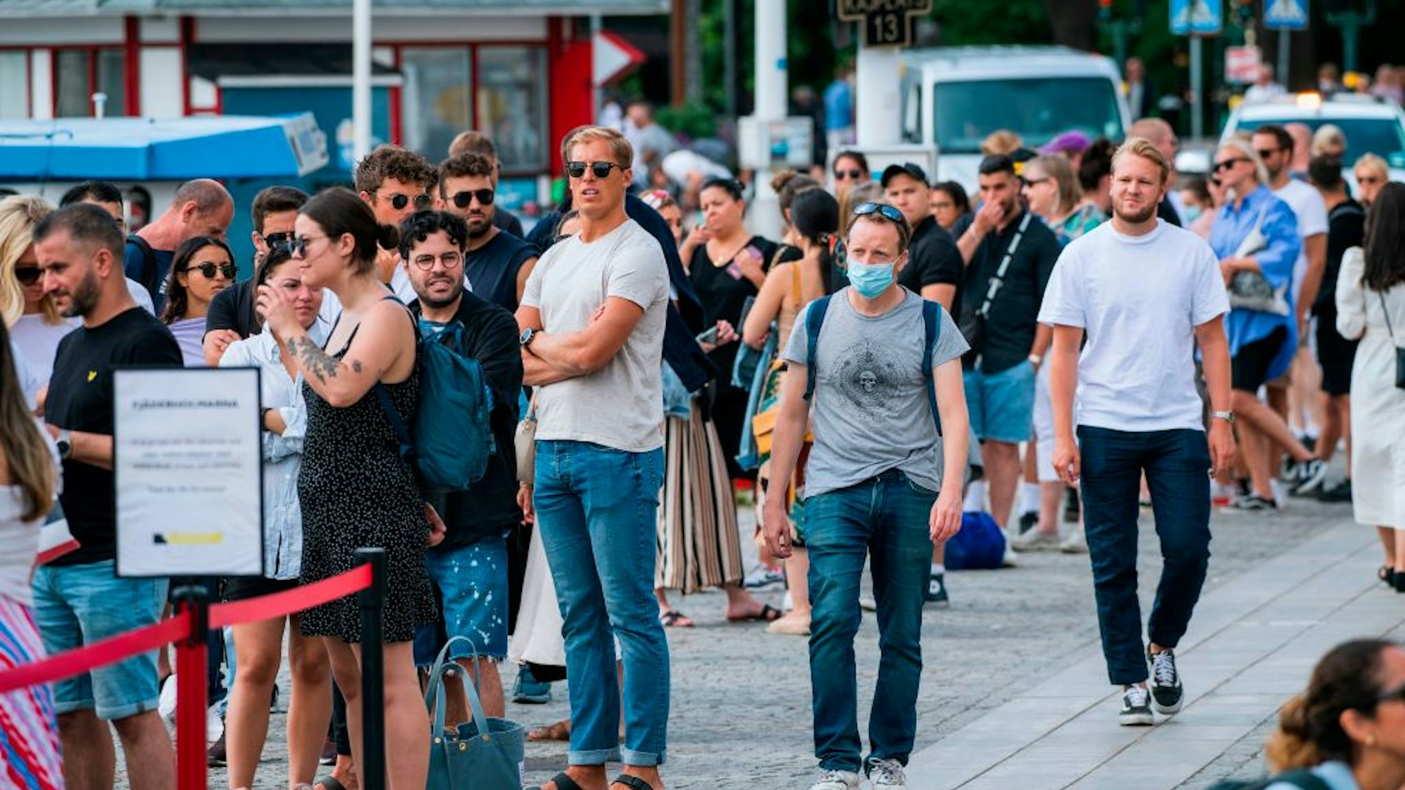 A man wearing a protective mask walks next to travellers as they queue up to board a boat at Stranvagen in Stockholm on July 27, 2020, during the novel coronavirus