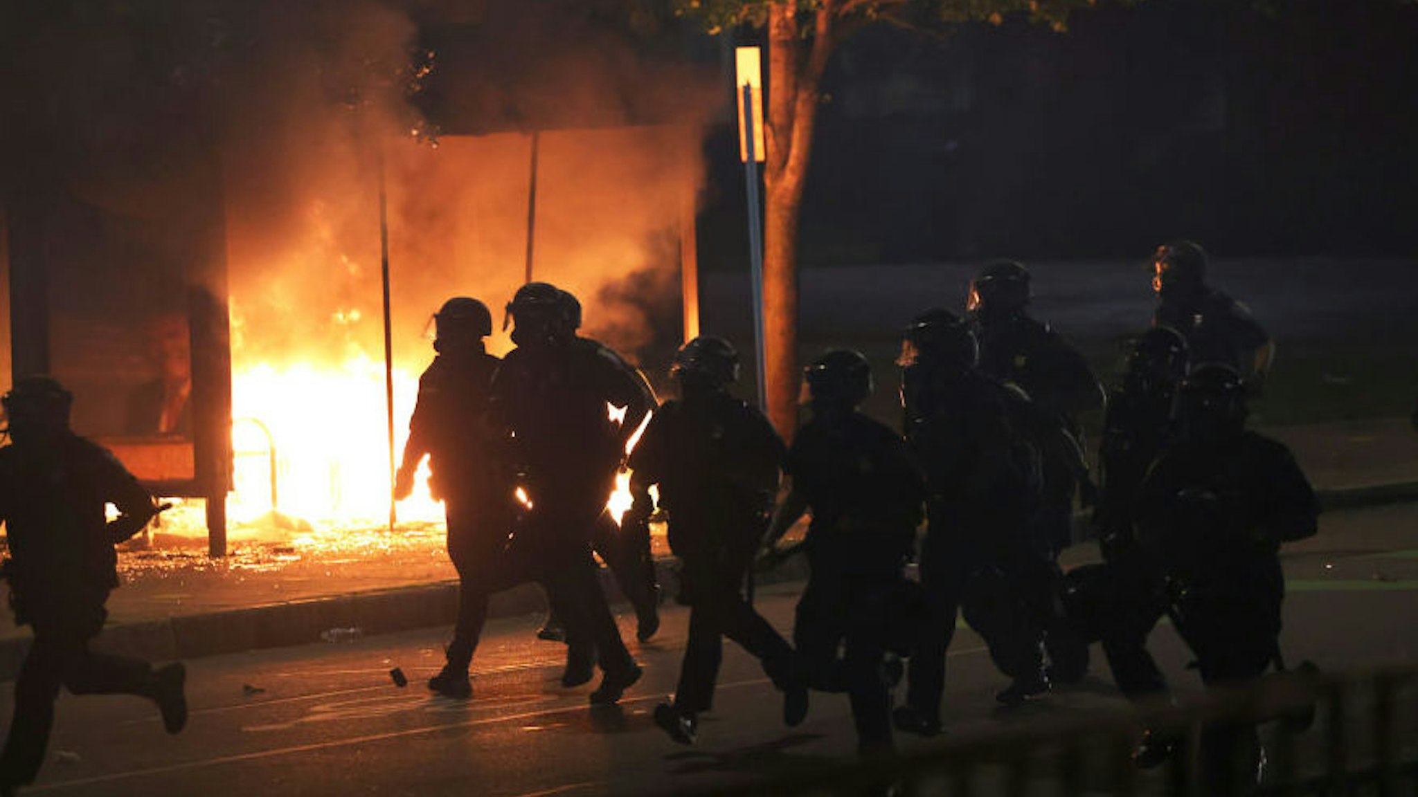 Police officers run past a bus station that was set on fire as they attempt to clear the streets after a march for Daniel Prude on September 04, 2020 in Rochester, New York.