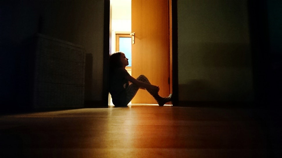 Backlit child sitting in a dark doorway in contemplation - stock photo