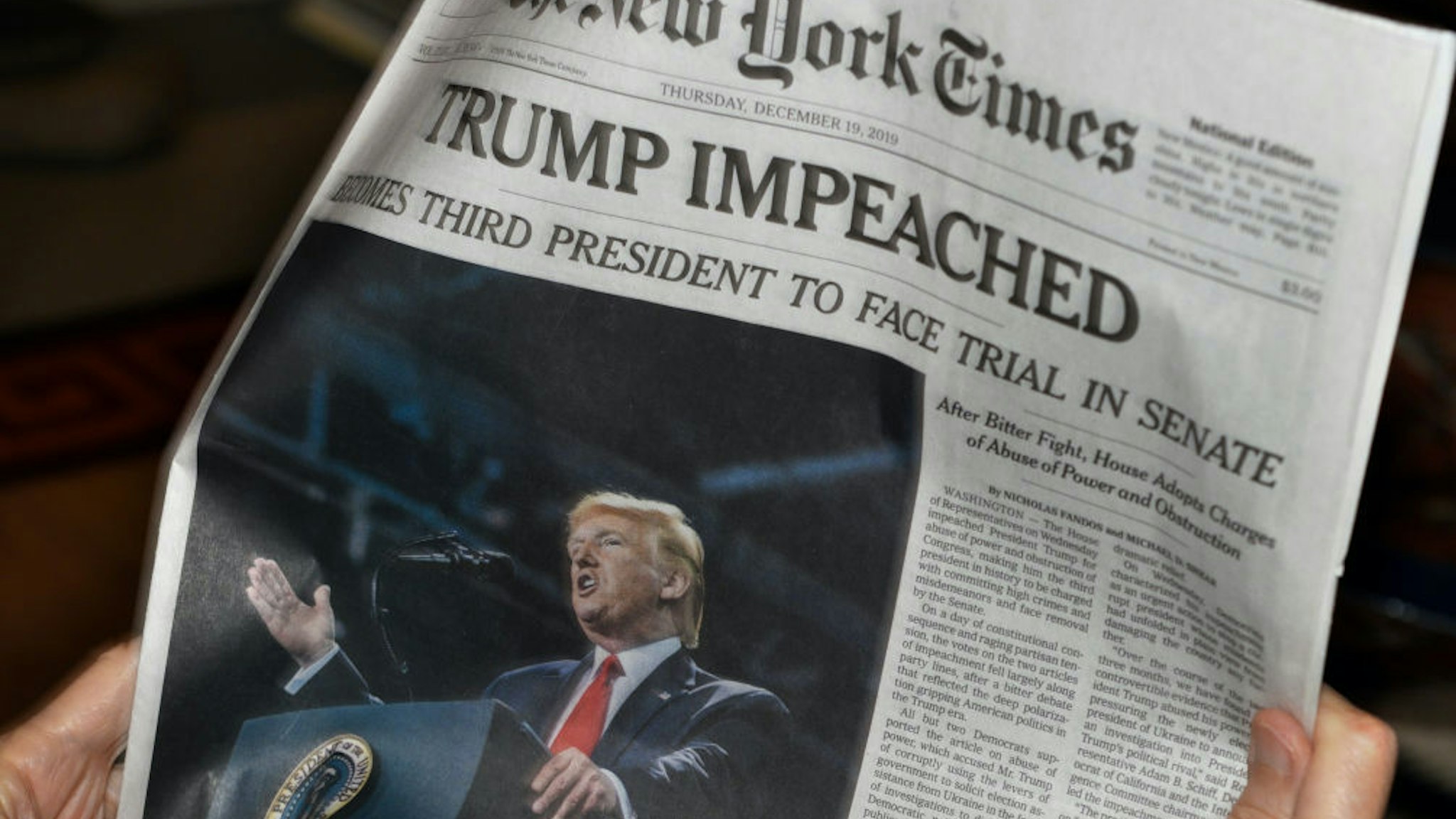 A woman reads the front page of the December 19, 2019 New York Times with its headline reporting the impeachment of U.S. President Donald Trump by the U.S. House of Representatives. (Photo by Robert Alexander/Getty Images)