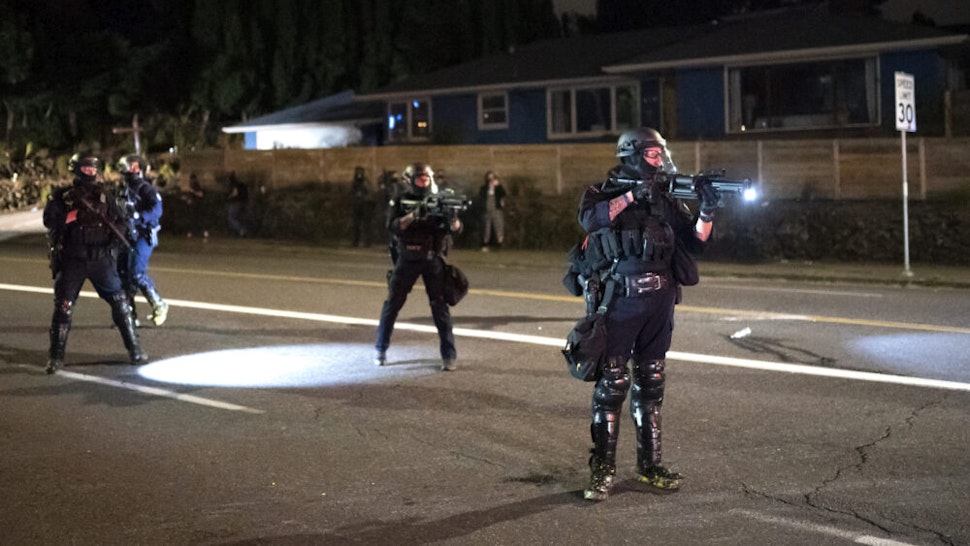 PORTLAND, OR - AUGUST 30: A Portland police officer points a less lethal weapon at anti-police protesters near the east police precinct a day after political violence left one person dead on August 30, 2020 in Portland, Oregon. City leaders asked for calm and time to conduct an investigation after a man was shot and killed near a pro-Trump rally on Saturday.
