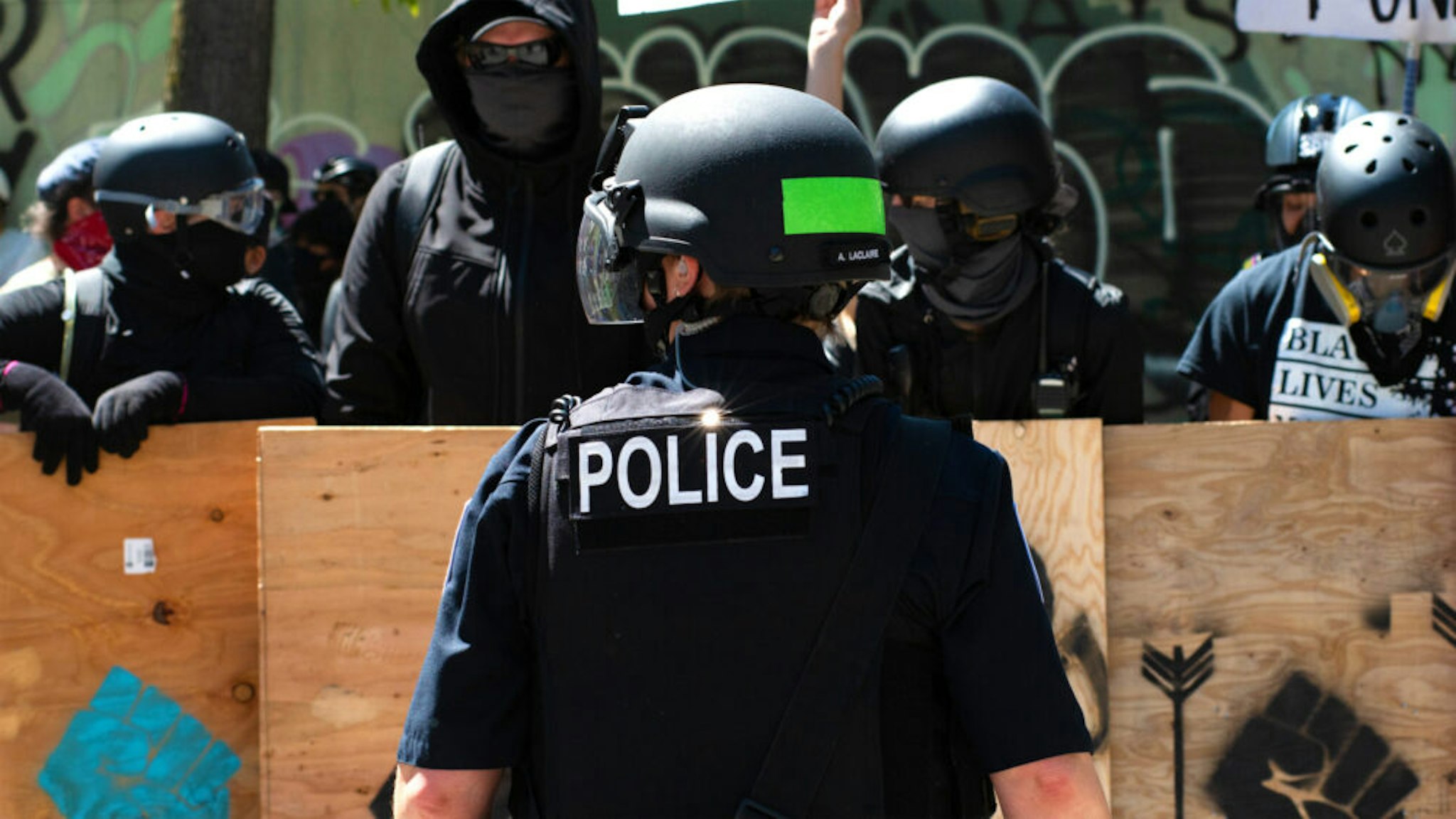 SEATTLE, WASHINGTON - AUGUST 9: A police officer stands in front of counter protesters during the Seattle Police Officers Guildâs rally to stop defunding of the Seattle Police Department on Sunday, August 9, 2020 at Seattle City Hall. The Seattle City Council passed a resolution to reduce the Seattle Police Department by up to 100 officers through layoffs but the council failed to pass a 50% cut of the Police Departmentâs remaining 2020 budget on August 5, 2020.
