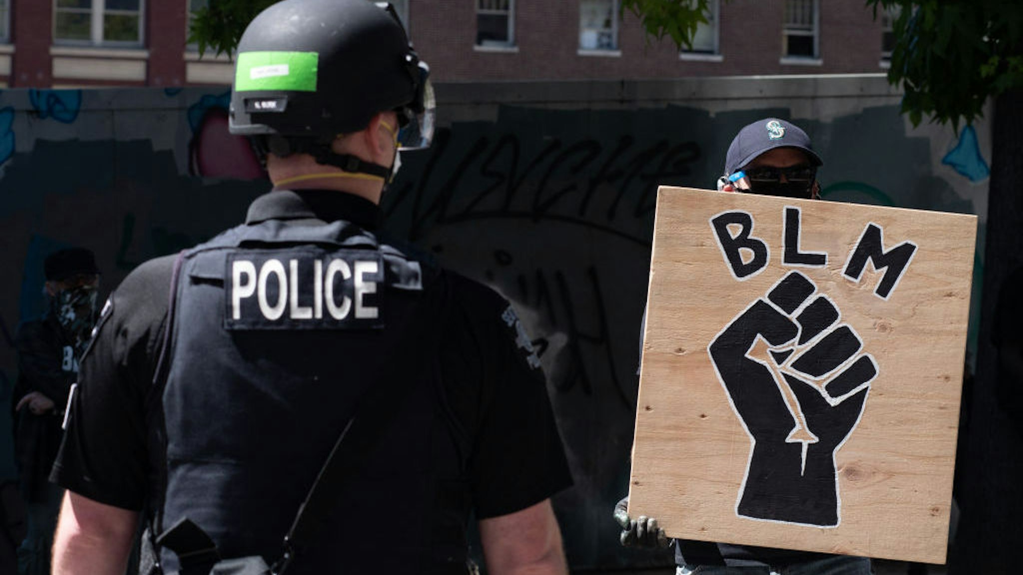 SEATTLE, WASHINGTON - AUGUST 9: A police officer stands in front of a Black Lives Matter sign during the Seattle Police Officers Guild√¢s rally to stop defunding of the Seattle Police Department on Sunday, August 9, 2020 at Seattle City Hall. The Seattle City Council passed a resolution to reduce the Seattle Police Department by up to 100 officers through layoffs but the council failed to pass a 50% cut of the Police Department√¢s remaining 2020 budget on August 5, 2020. (Photo by Noah Riffe/Anadolu Agency via Getty Images)