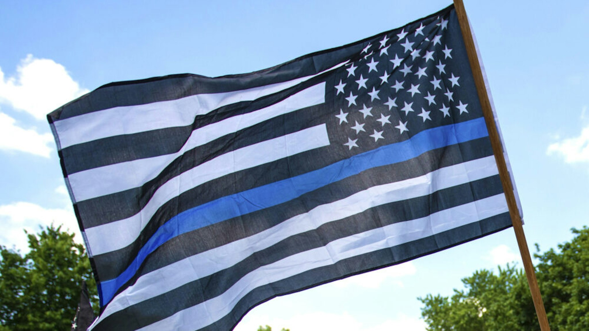 A demonstrator holds a "Thin Blue Line" flag and a sign in support of police during a protest outside the Governors Mansion on June 27, 2020 in St Paul, Minnesota. A group called "Bikers for 45" advocating a pro-police stance arranged the protest and were met with counter-protesters calling for measures to defund police.