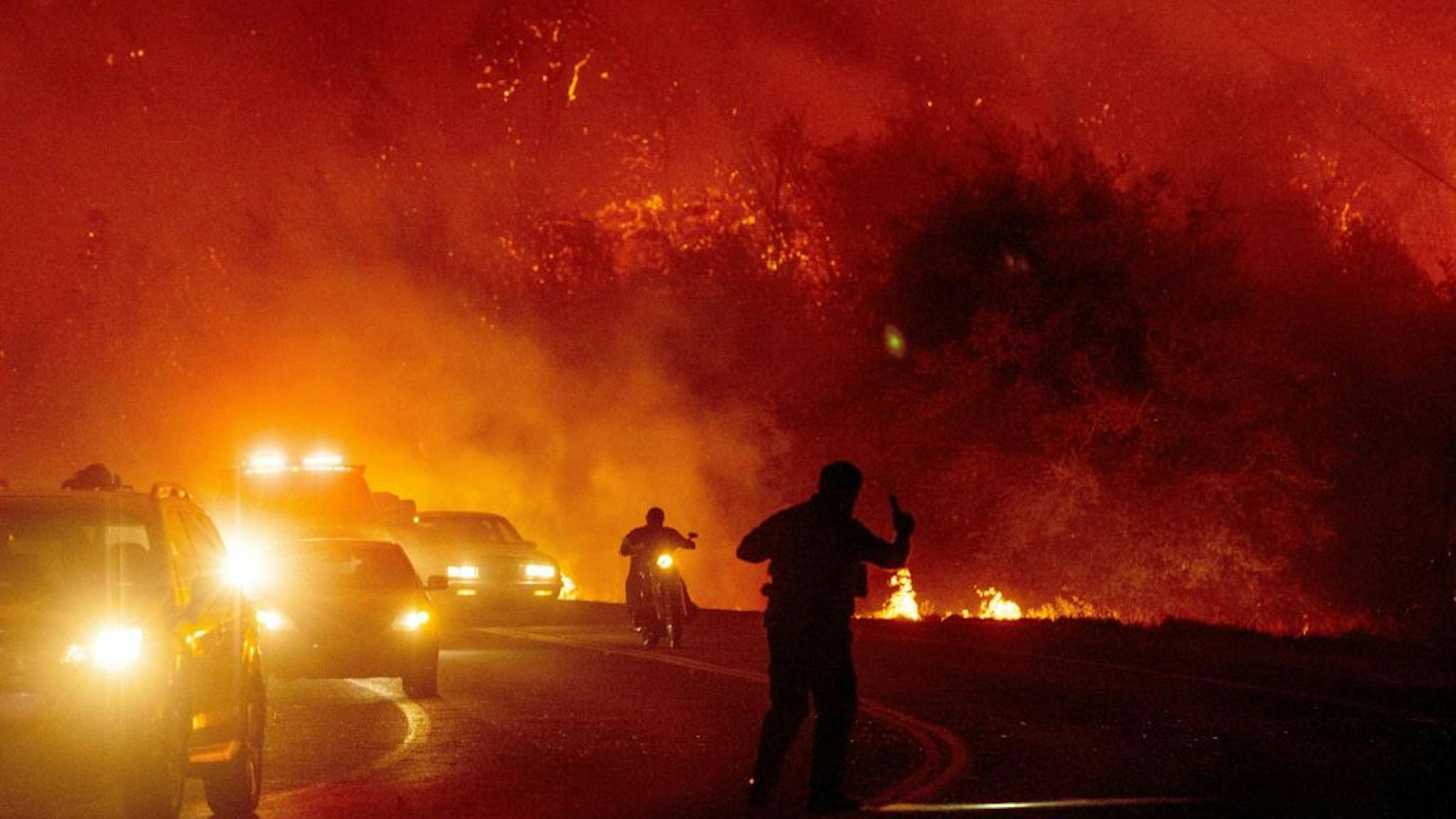 A law enforcement officer guides evacuees down a road surrounded by fire at the Bear fire in Oroville, California on September 9, 2020. - Dangerous dry winds whipped up California's record-breaking wildfires and ignited new blazes, as hundreds were evacuated by helicopter and tens of thousands were plunged into darkness by power outages across the western United States.