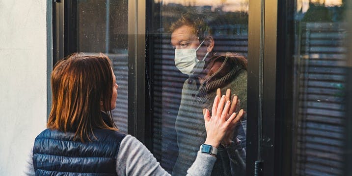Woman looking at masked husband quarantined behind window