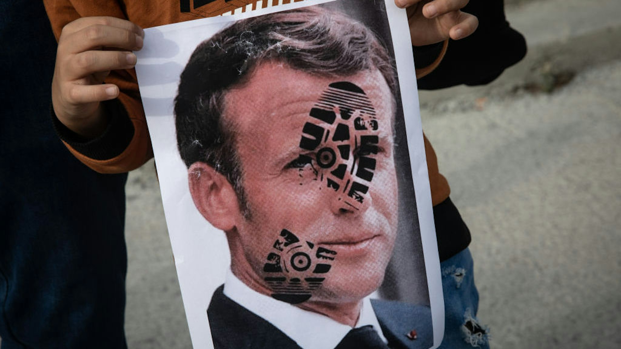 ISTANBUL, TURKEY - OCTOBER 25: A boy holds a poster showing the portrait of French President Emmanuel Macron during a protest against French president Emmanuel Macron on October 25, 2020 in Istanbul, Turkey. People gathered to protest against the recent statements by French President Emmanuel Macron regarding the beheading of a teacher that displayed cartoons of Prophet Muhammad in his class and the closure of some mosques in France. (Photo by Chris McGrath/Getty Images)