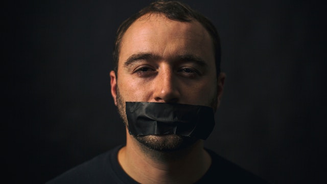 Portrait Of Man With Tape On Mouth Against Black Background