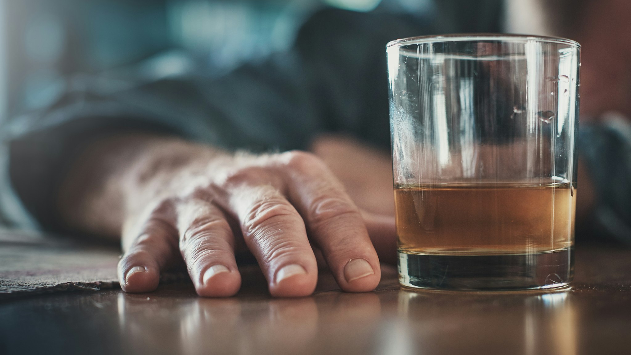 Hand by glass of liquor, man's head on table - stock photo