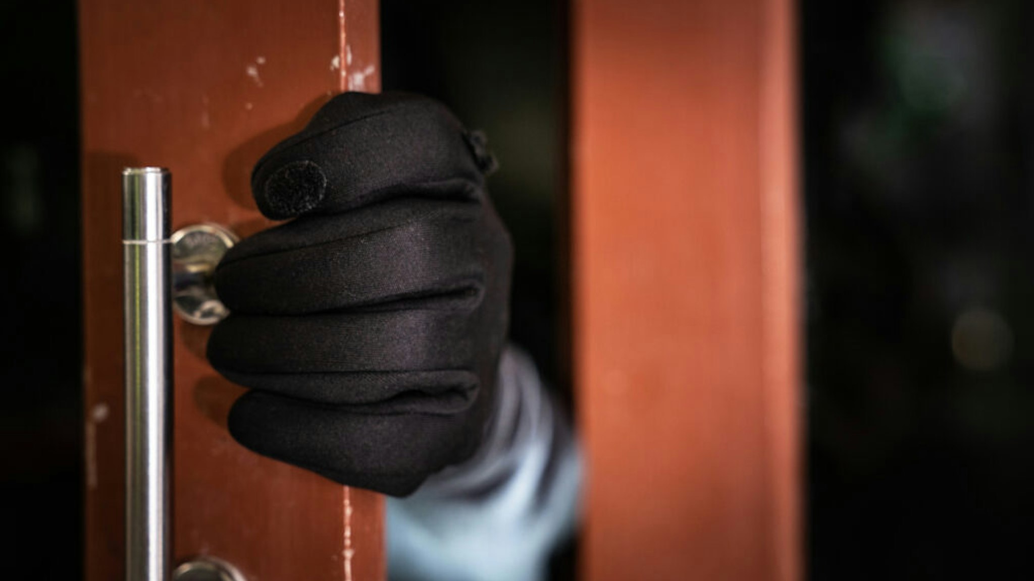 dangerous masked burglar with crowbar breaking into a victim's home door,