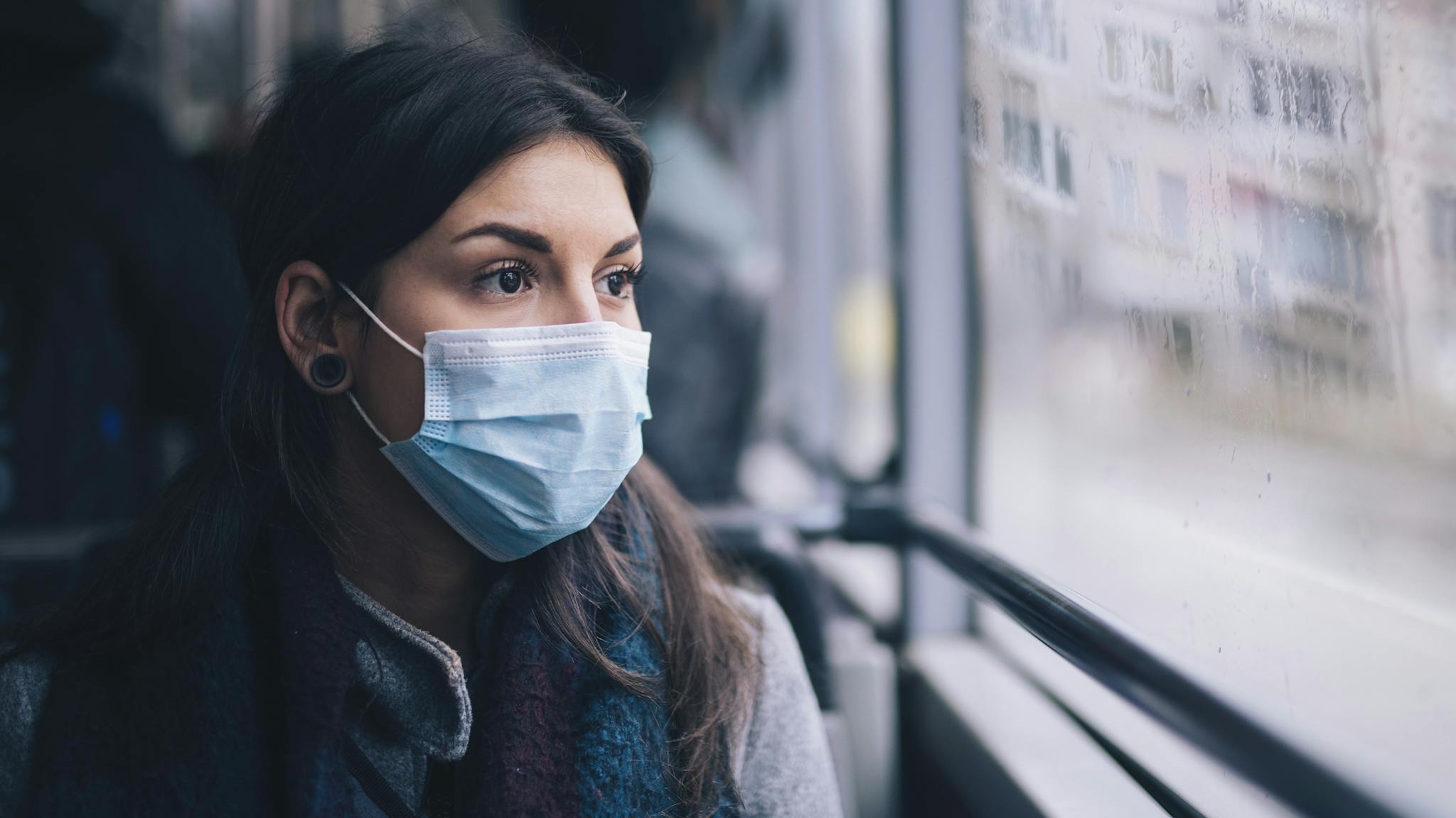Worried Woman With Protective Face Mask In Bus Transport. Young woman wearing protective face mask, she sitting in bus transportation in the city.