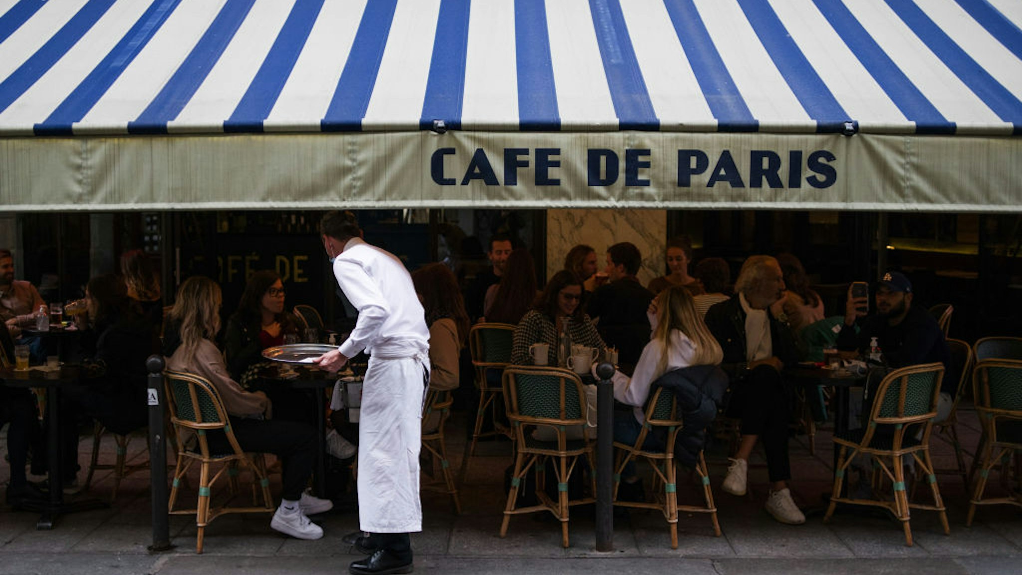 A waiter serves customers eating and drinking on the terrace area outside Cafe de Paris, ahead of the enforcement of new Covid-19 restrictions which will see bars and restaurants closing early, in Paris, France, on Monday, Sept. 28, 2020. President Emmanuel Macrons government is seeking to ease tension after the first significant tightening of restrictions on French daily life since the end of the lockdown in May. Photographer: Nathan Laine/Bloomberg via Getty Images