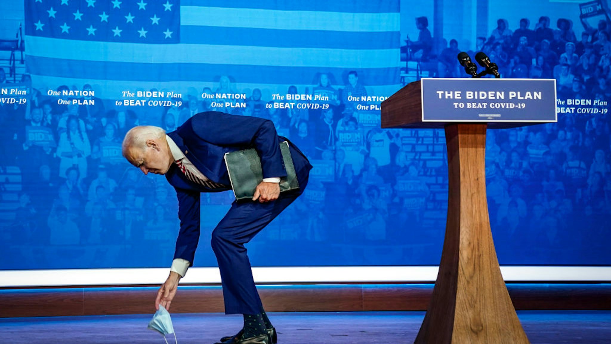 Democratic presidential nominee Joe Biden picks up his protective face mask after he dropped it while leaving the stage following his remarks for combatting the coronavirus pandemic at The Queen theater on October 23, 2020 in Wilmington, Delaware.