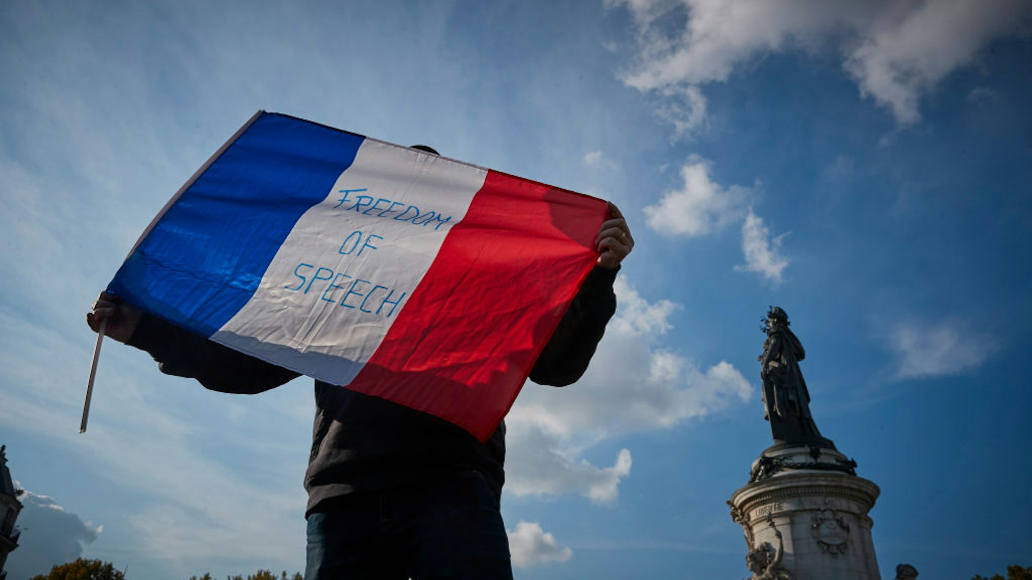 PARIS, FRANCE - OCTOBER 18: A protestor waves a French Tricolor flag with 'Freedom of Speech' written on it during an anti-terrorism vigil at Place de La Republique for the murdered school teacher Samuel Paty who was killed in a terrorist attack in the suburbs of Paris on October 18, 2020 in Paris, France. Thousands of people turned out to show solidarity and express their support for freedom of speech in the wake of Friday's attack. France launched an anti-terrorism investigation after the October 16 incident where police shot the 18 year-old assailant who decapitated the history-geography teacher for having shown a caricature of prophet Mohamed as an example of freedom of speech at the College Bois d'Aulne middle-school. (Photo by Kiran Ridley/Getty Images)
