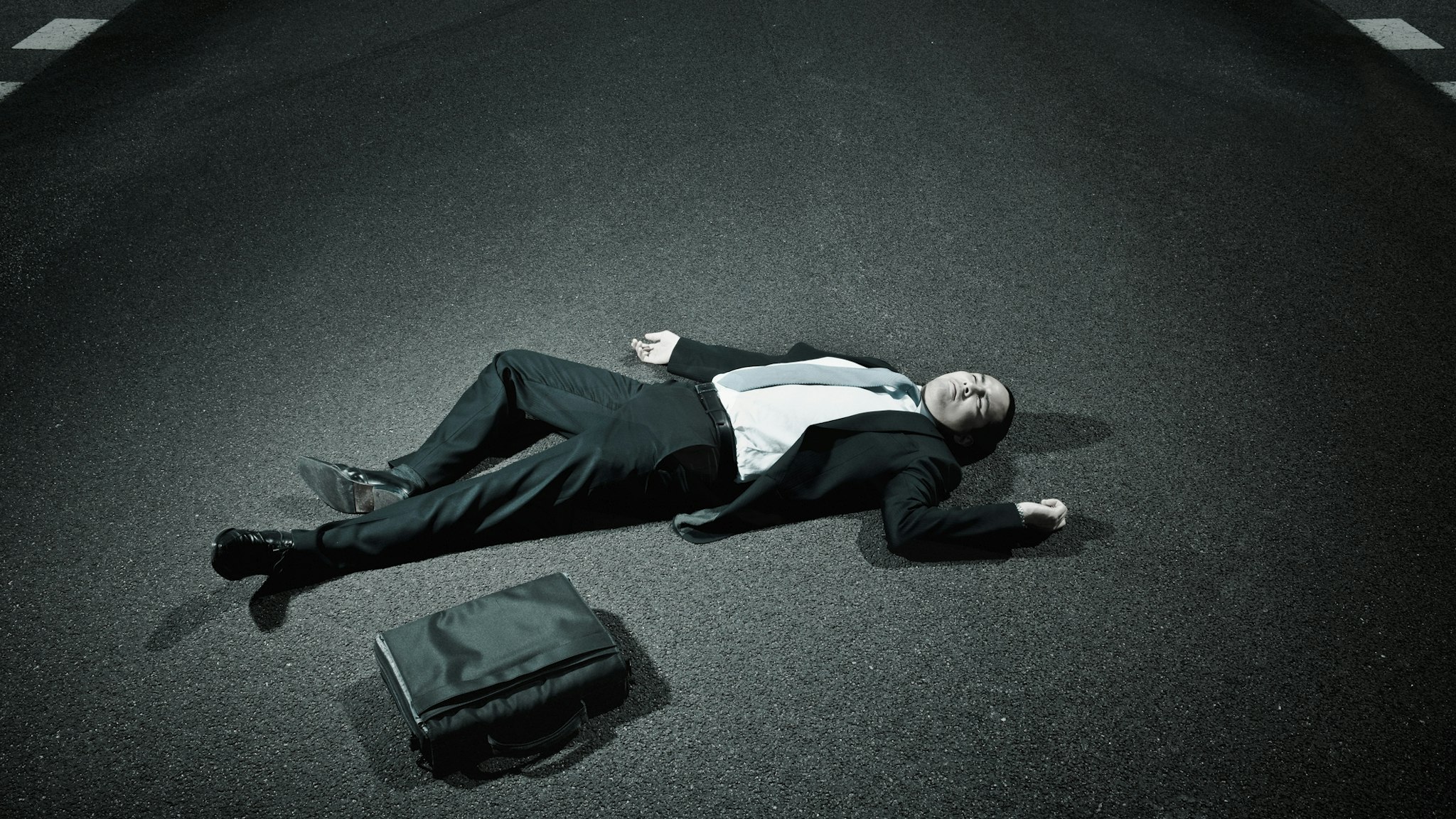 businessman laying on asphalt roadway - stock photo