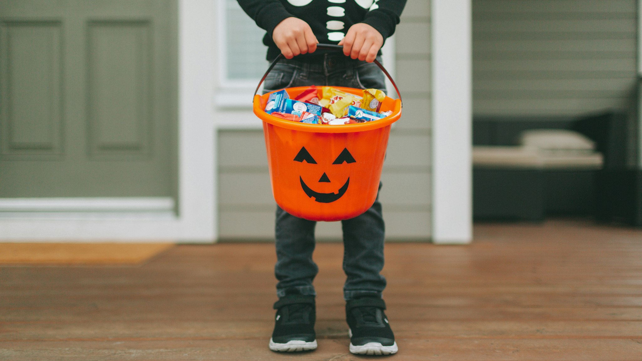 Boy With Sweet Food In Bucket Standing At Home During Halloween