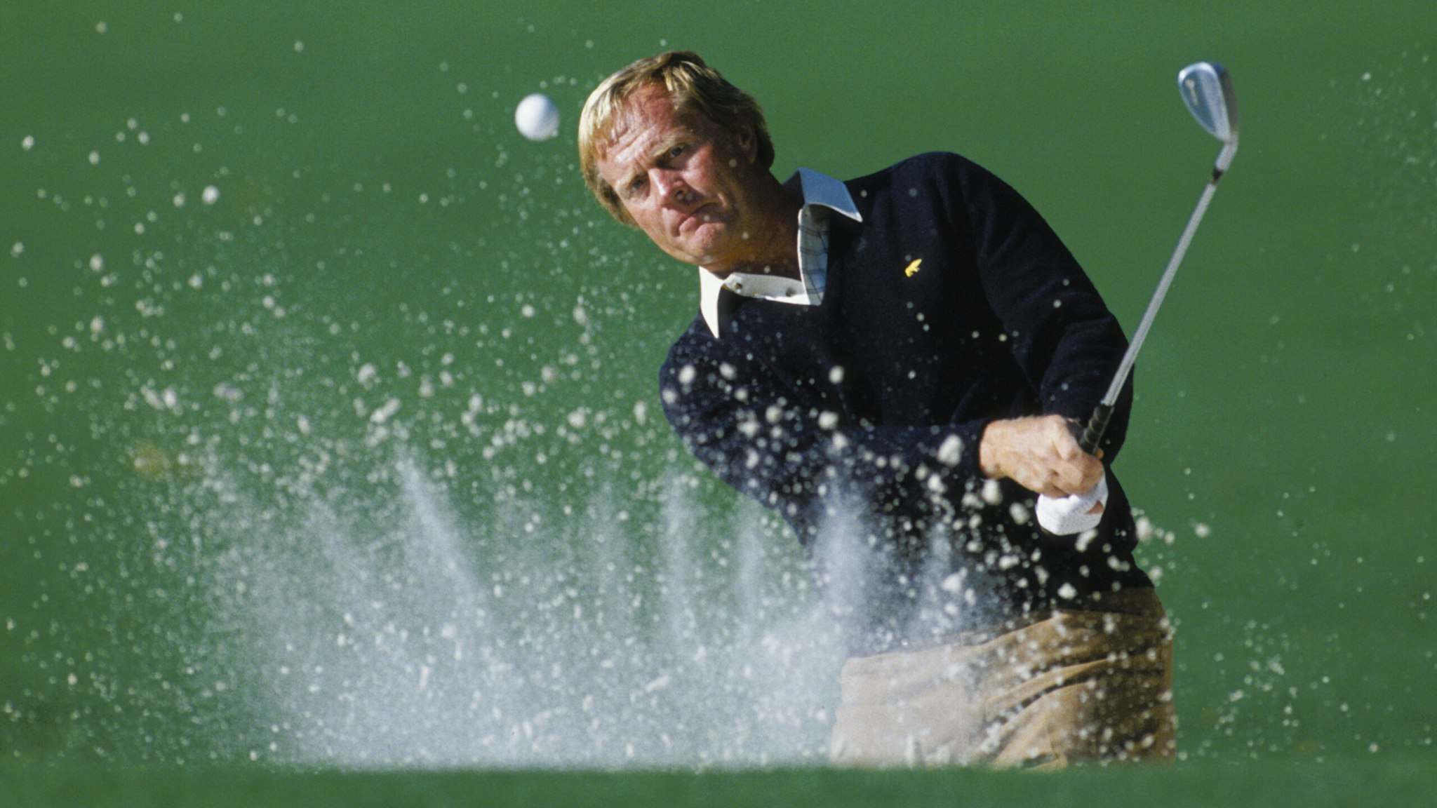 Jack Nicklaus of the USA keeps his eye on the ball as he hits out of the bunker with the sand creating a crown effect during the US Masters Golf Tournament on 12th April 1986 at the Augusta National Golf Club in Augusta, Georgia, USA. Visions of Sports.