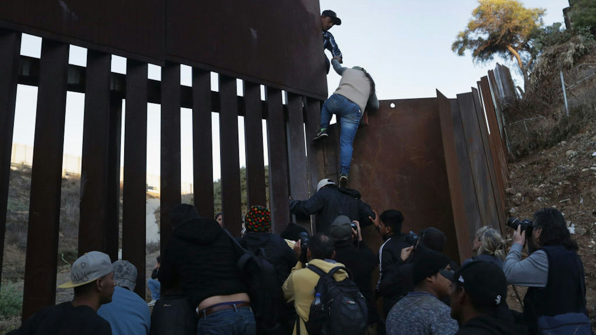 A woman climbs atop a fellow member of the migrant caravan while crossing over the U.S.-Mexico border fence on December 2, 2018 from Tijuana, Mexico. Numerous members of the caravan were able to pass from Tijuana to San Diego and were quickly taken into custody by U.S. Border Patrol agents. Most had planned to request political asylum in the United States after traveling more than 6 weeks from Central America. (Photo by John Moore/Getty Images)