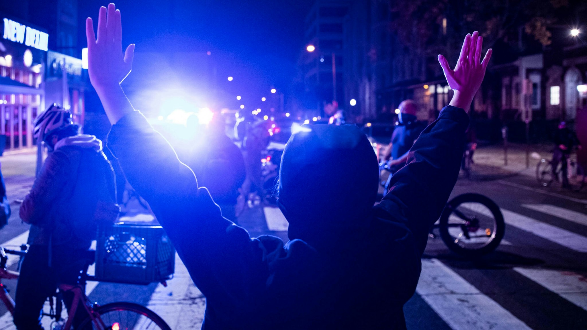 A protester raises their hands in West Philadelphia on October 27, 2020, during a demonstration against the fatal shooting of 27-year-old Walter Wallace, a Black man, by police. - Hundreds of people demonstrated in Philadelphia late on October 27, with looting and violence breaking out in a second night of unrest after the latest police shooting of a Black man in the US. The fresh unrest came a day after the death of 27-year-old Walter Wallace, whose family said he suffered mental health issues. On Monday night hundreds of demonstrators took to the streets, with riot police pushing them back with shields and batons.