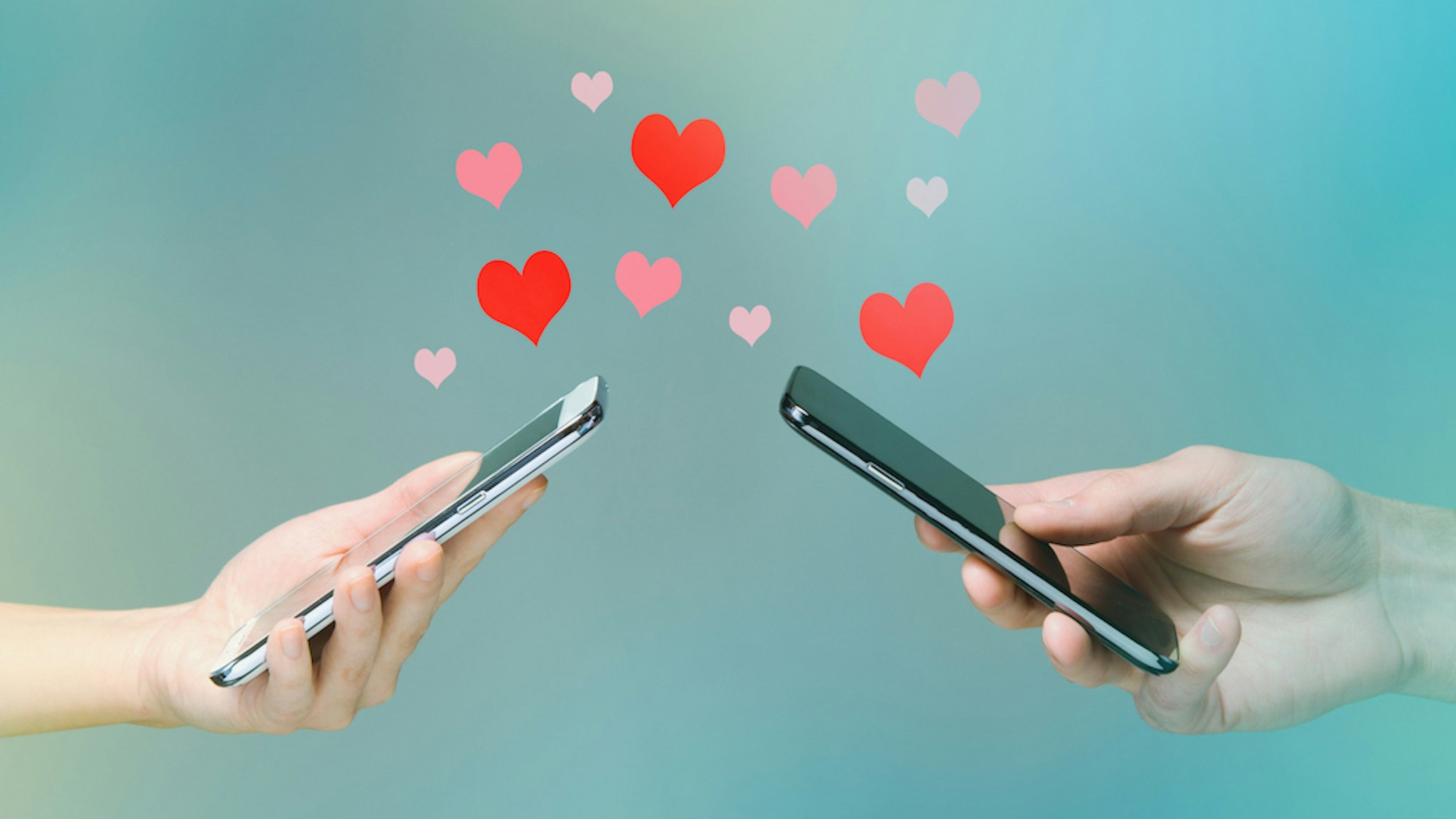 Young man and woman's hands holding smart phones with hearts floating over (PM Images/Getty Images)