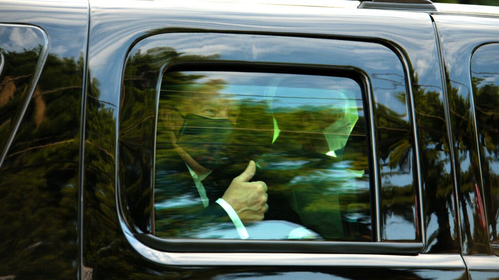 U.S. President Donald Trump wears a protective mask while giving a thumbs up as he is driven in a motorcade past supporters outside of Walter Reed National Military Medical Center in Bethesda, Maryland, U.S., on Sunday, Oct. 4, 2020. Trump briefly left his hospital in a car to greet supporters gathered outside, after posting a video on Twitter saying he was about to make a surprise visit.