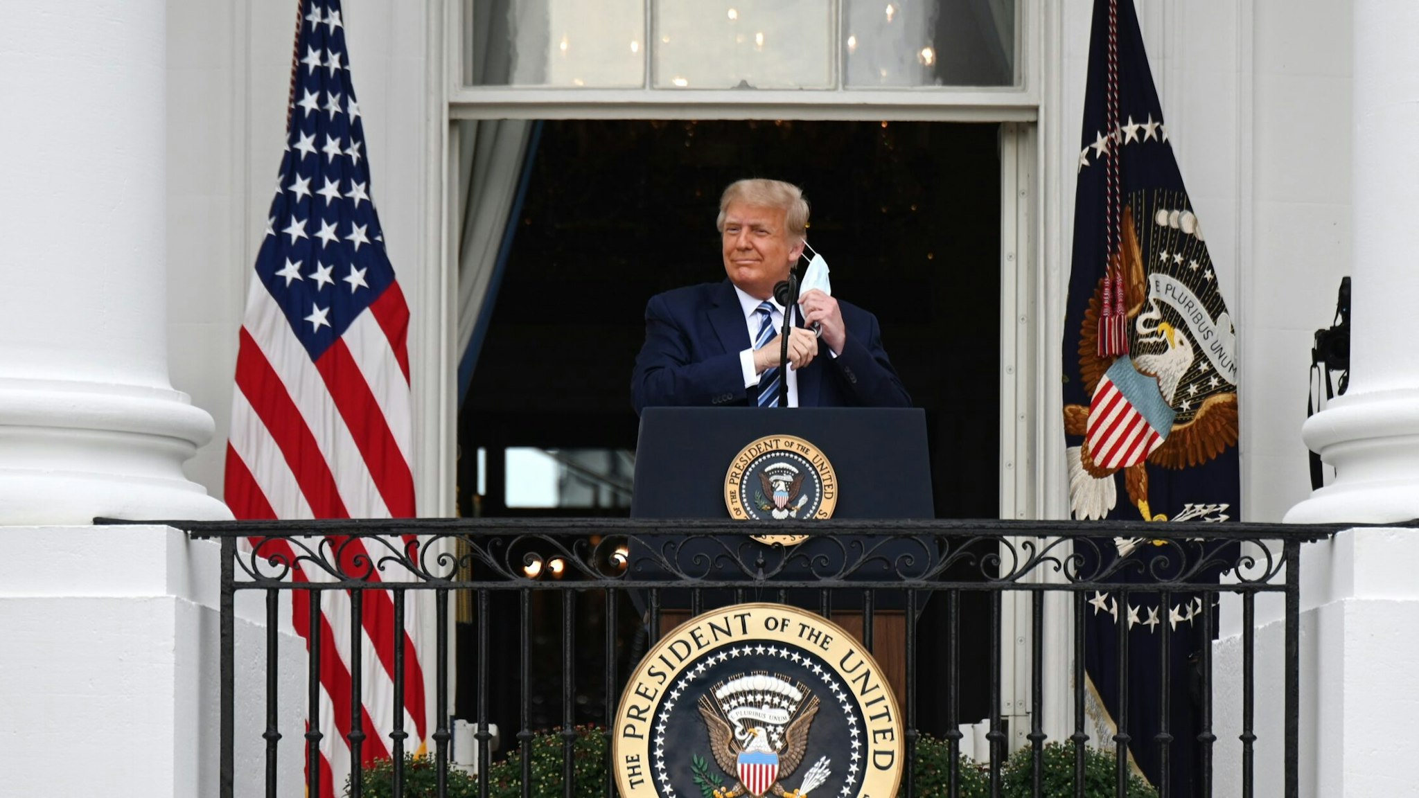U.S. President Donald Trump removes a protective mask ahead of speaking from the Truman Balcony of the White House in Washington, D.C., U.S., on Saturday, Oct. 10, 2020. Trump, making his first public appearance since returning from a three-day hospitalization for Covid-19, is setting the stage for a return to the campaign trail even as questions remain about whether hes still contagious. Photographer: