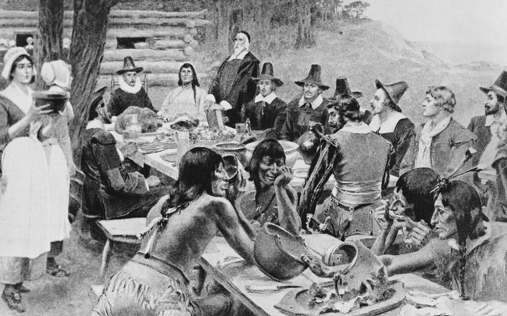 A depiction of early settlers of the Plymouth Colony sharing a harvest Thanksgiving meal with members of the local Wampanoag tribe at the Plymouth Plantation, Plymouth, Massachusetts, 1621.