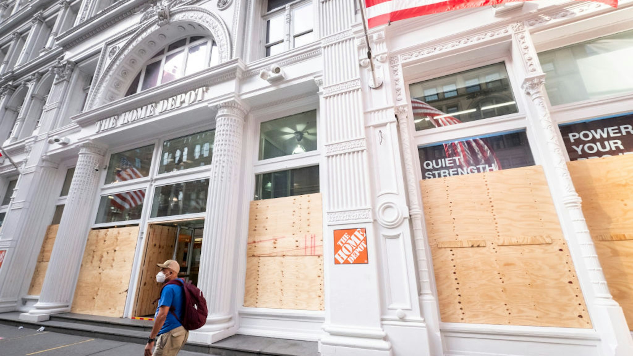 A man wearing a mask walks past a Home Depot on 5th Avenue Manhattan that is open for business but has all of their windows boarded up to prevent anyone from vandalizing or looting the store.