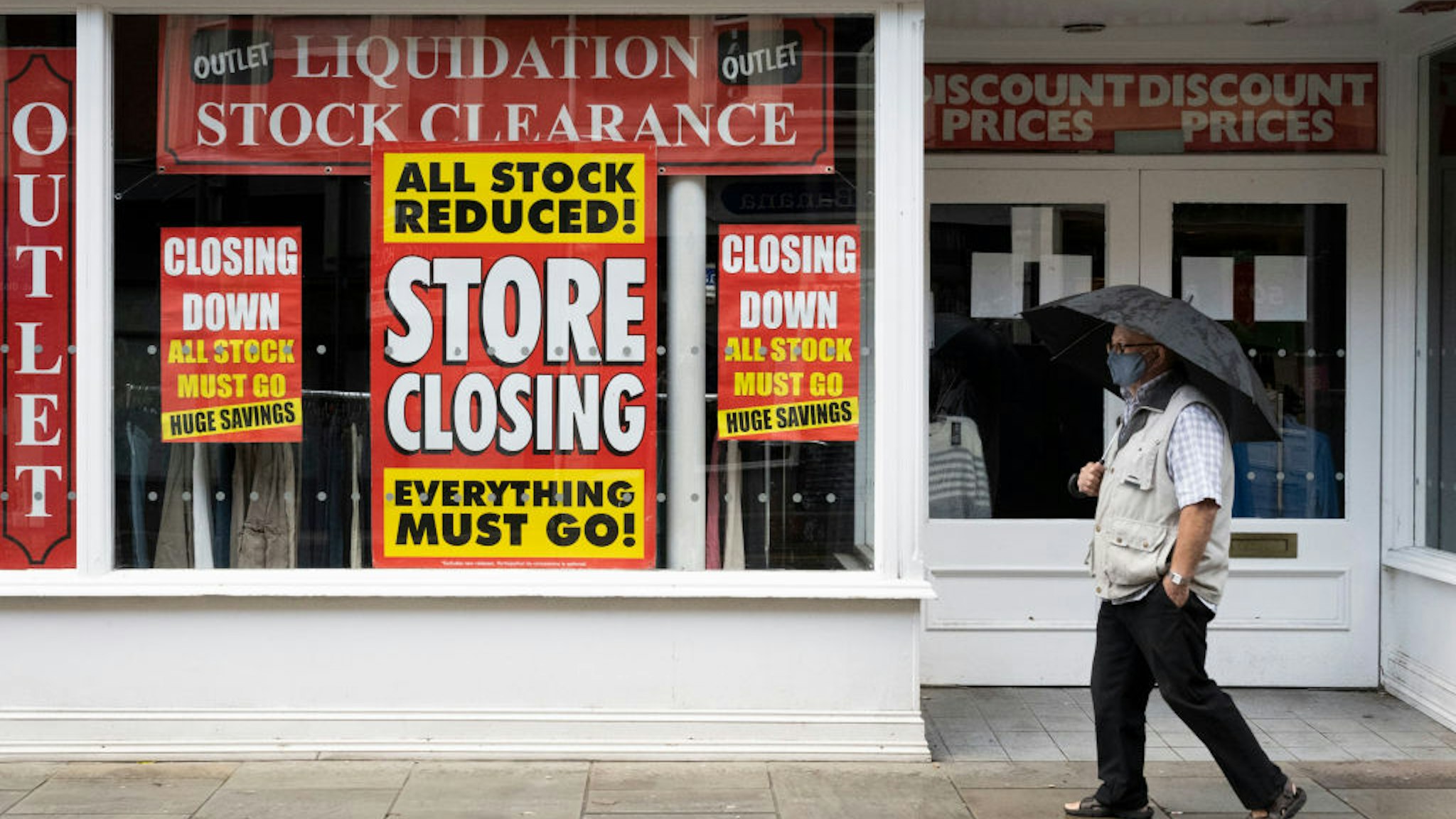 A man wearing a face mask walks past a shop with signs in the window saying its closing down in Newport town centre on October 31, 2020 in Newport, Wales.